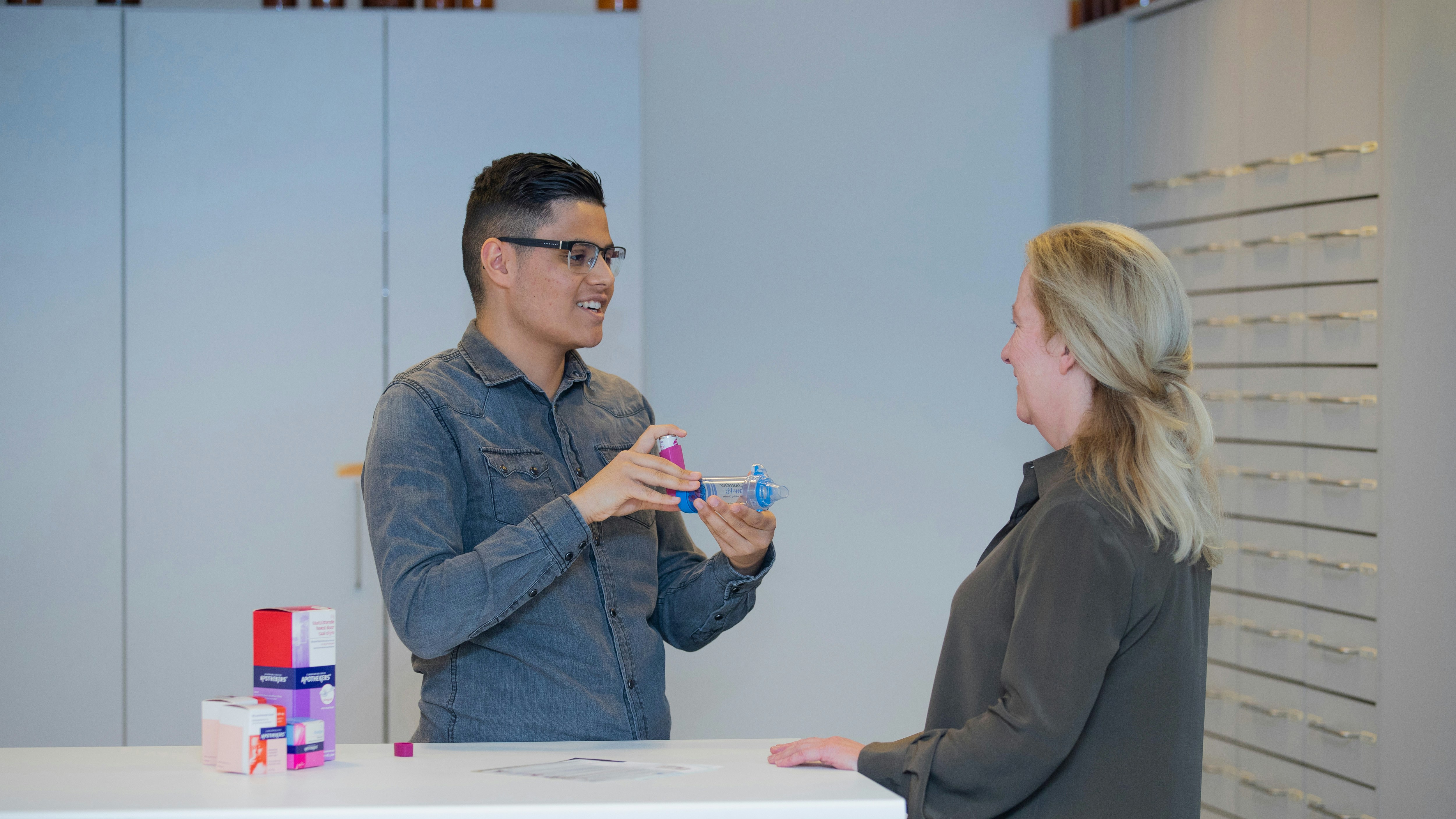 jongen achter een balie geeft medicijnen aan een vrouw