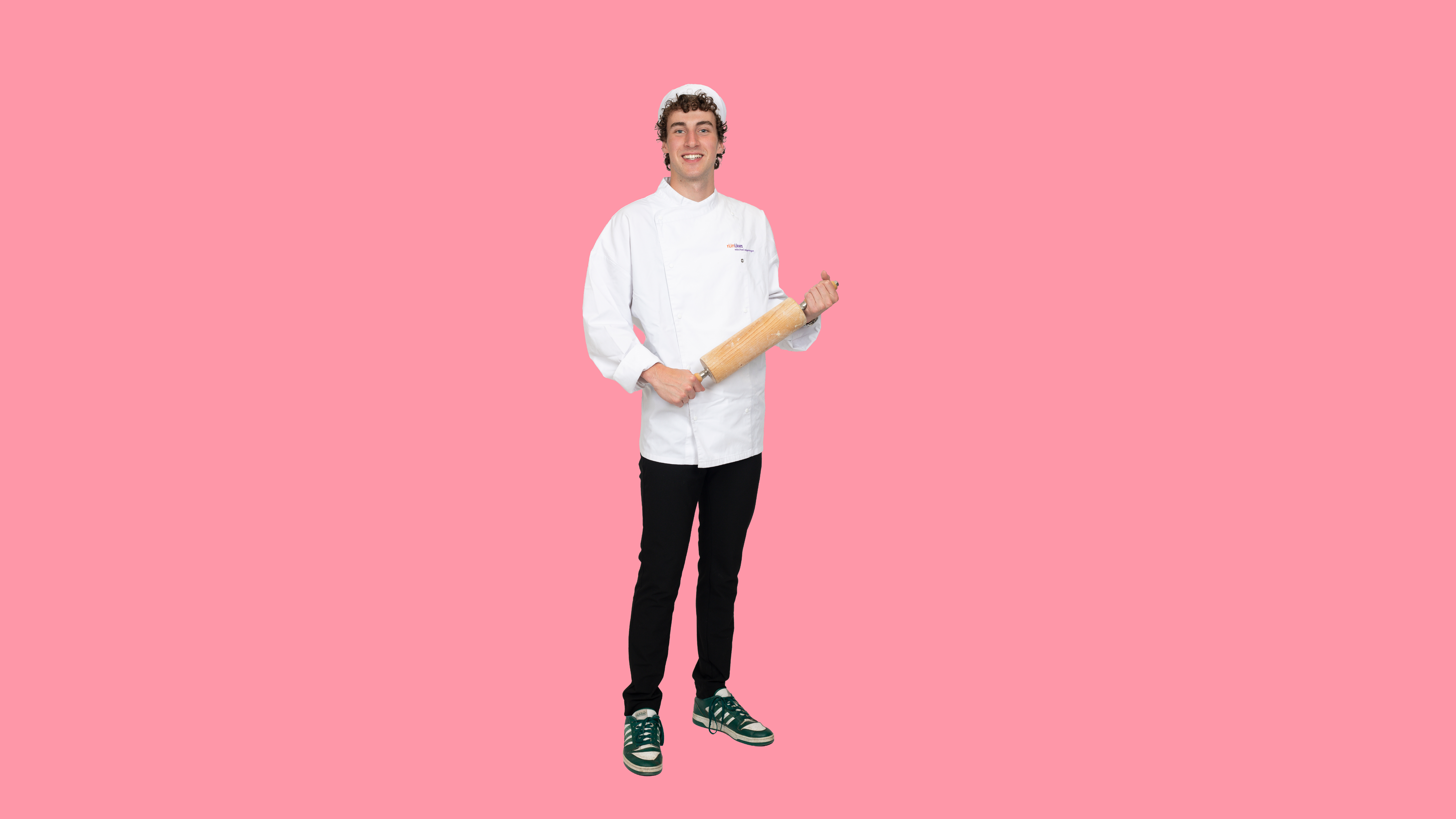 Jongen in bakkerskleding houdt een deegroller vast en kijkt in de camera
