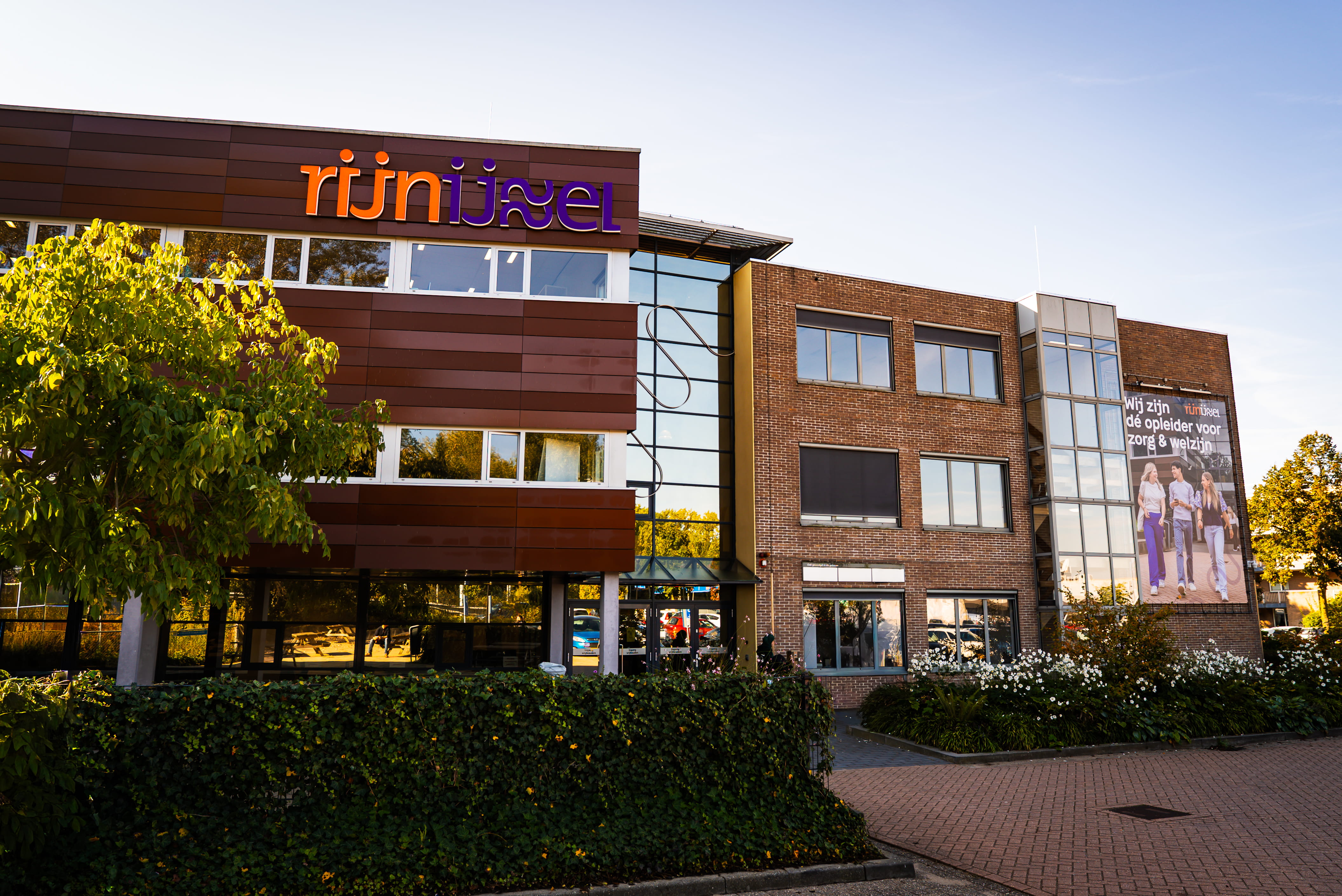 Je ziet een bruin gebouw met veel ramen en Rijn IJssel op de voorkant