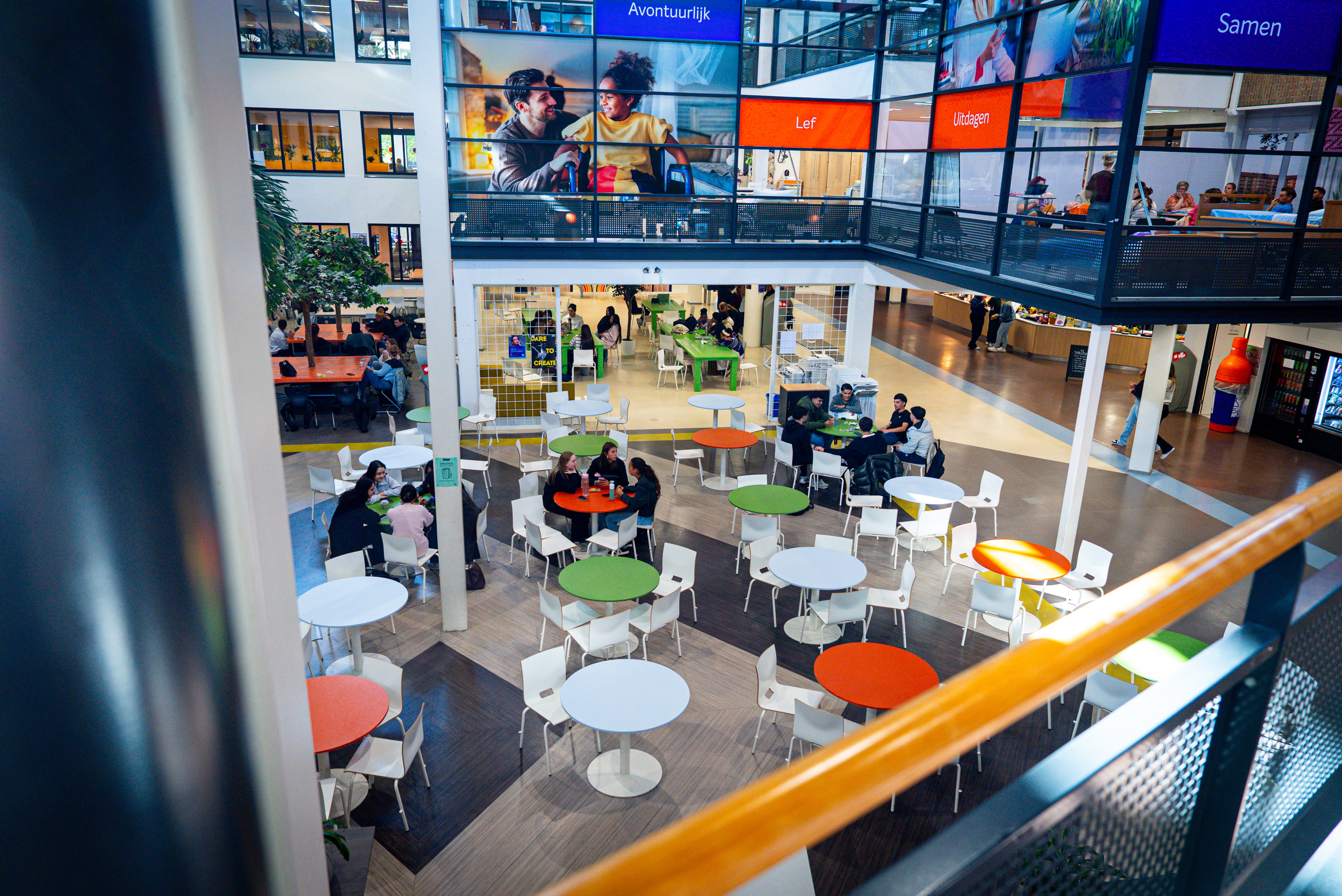 Je ziet aula van een school met tafels en stoelen van boven gefotografeert