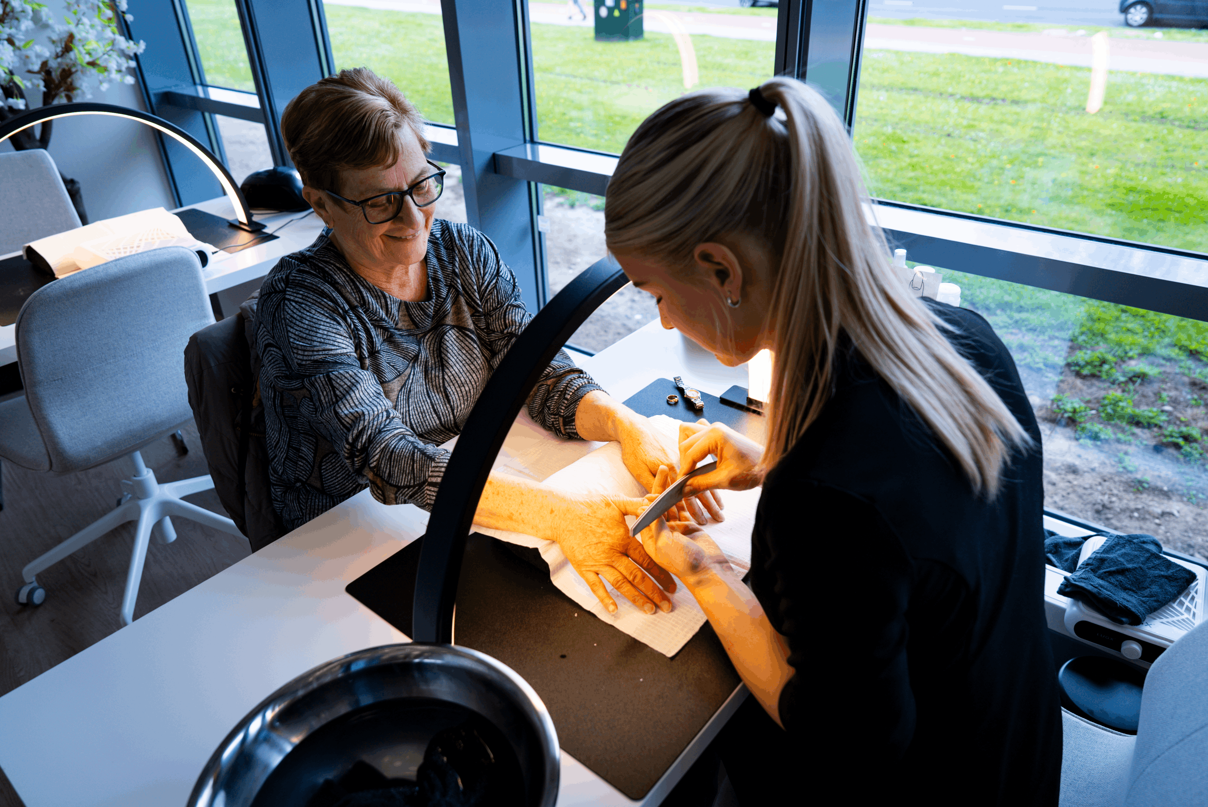 Meisje is bezig om de nagels van een vrouw aan het vijlen onder een lamp