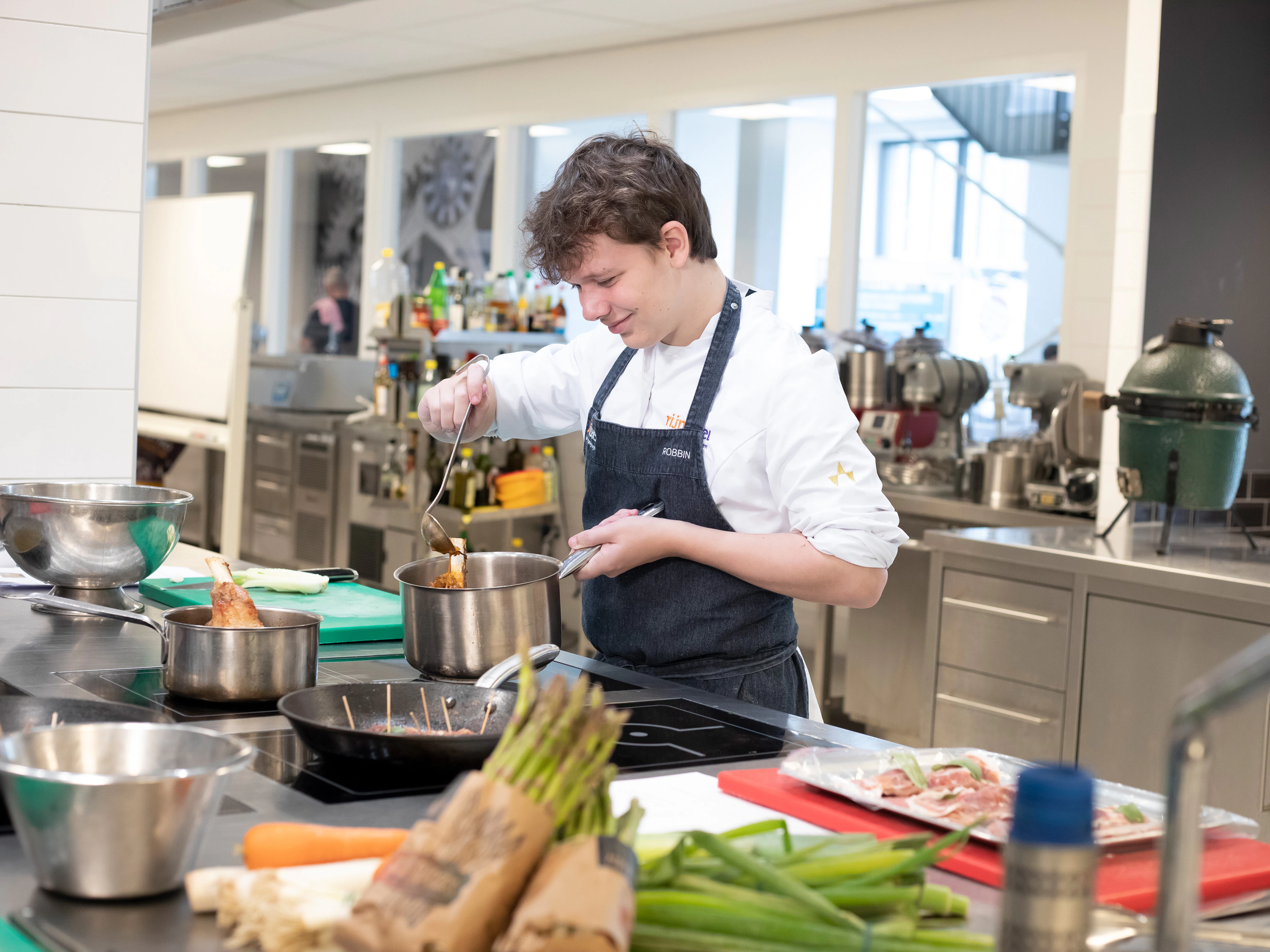 Jongen in kokskleding is aan het koken met een steelpan