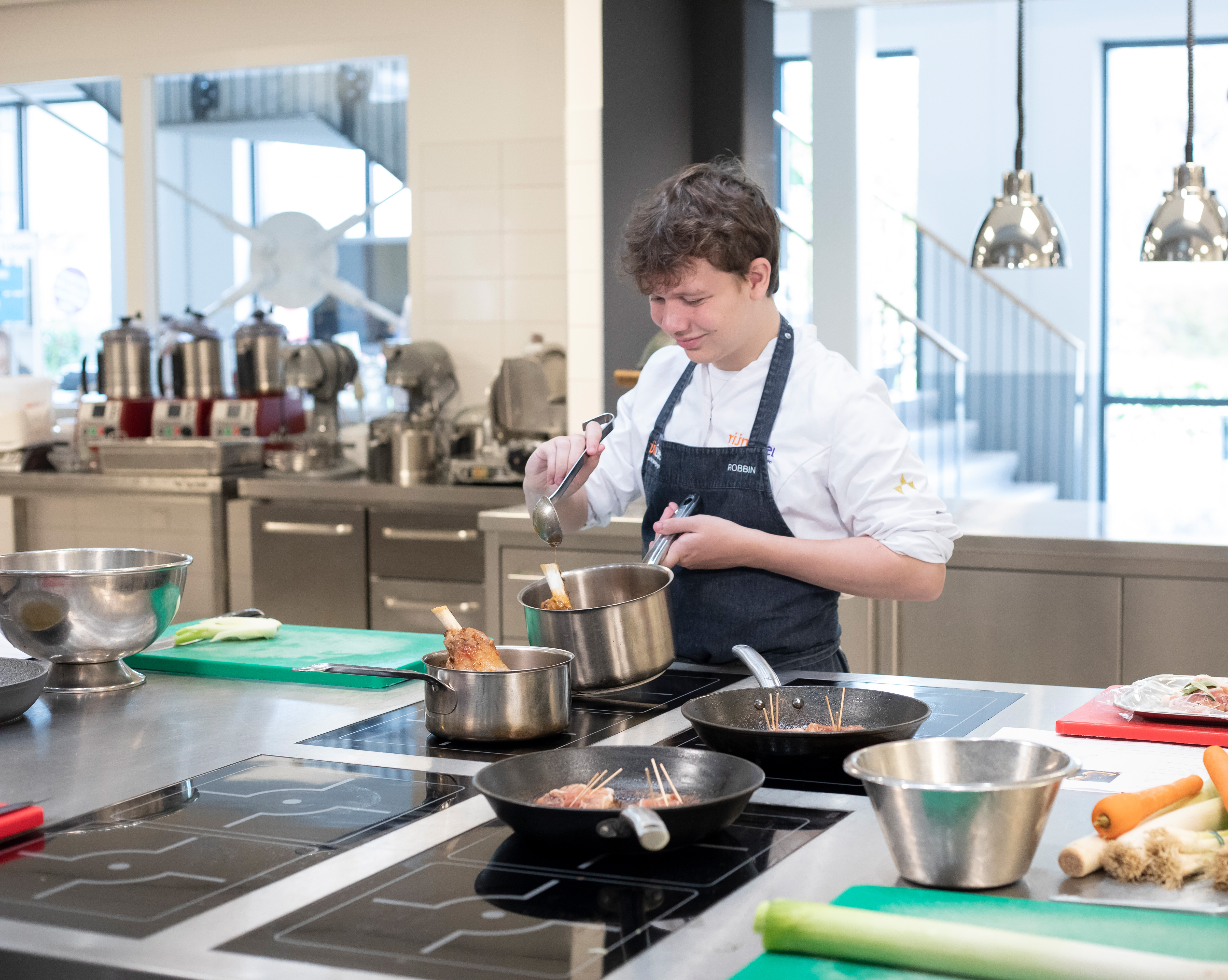 Jongen in kokskleding is aan het koken met een steelpan