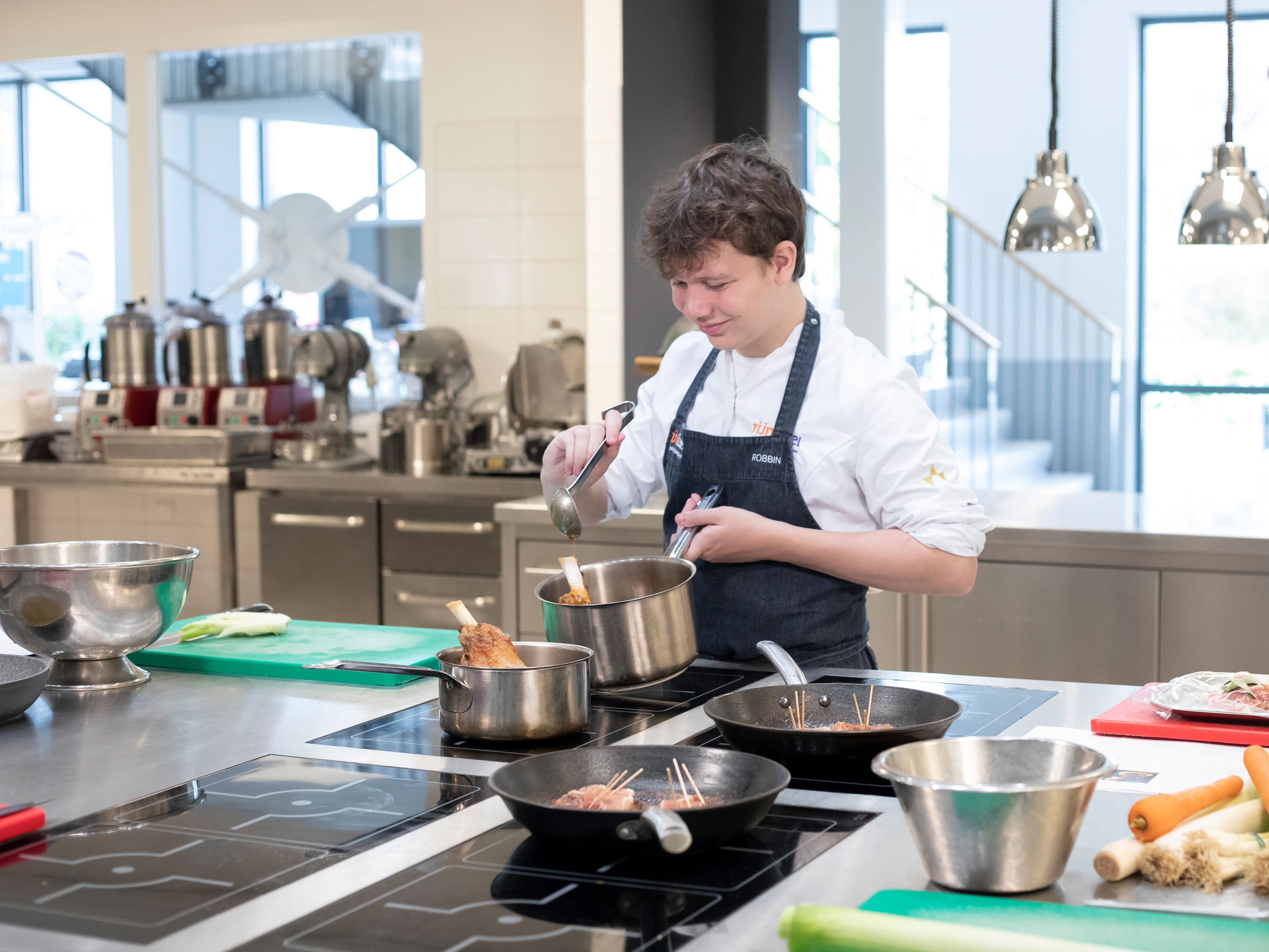 Jongen in kokskleding is aan het koken met een steelpan