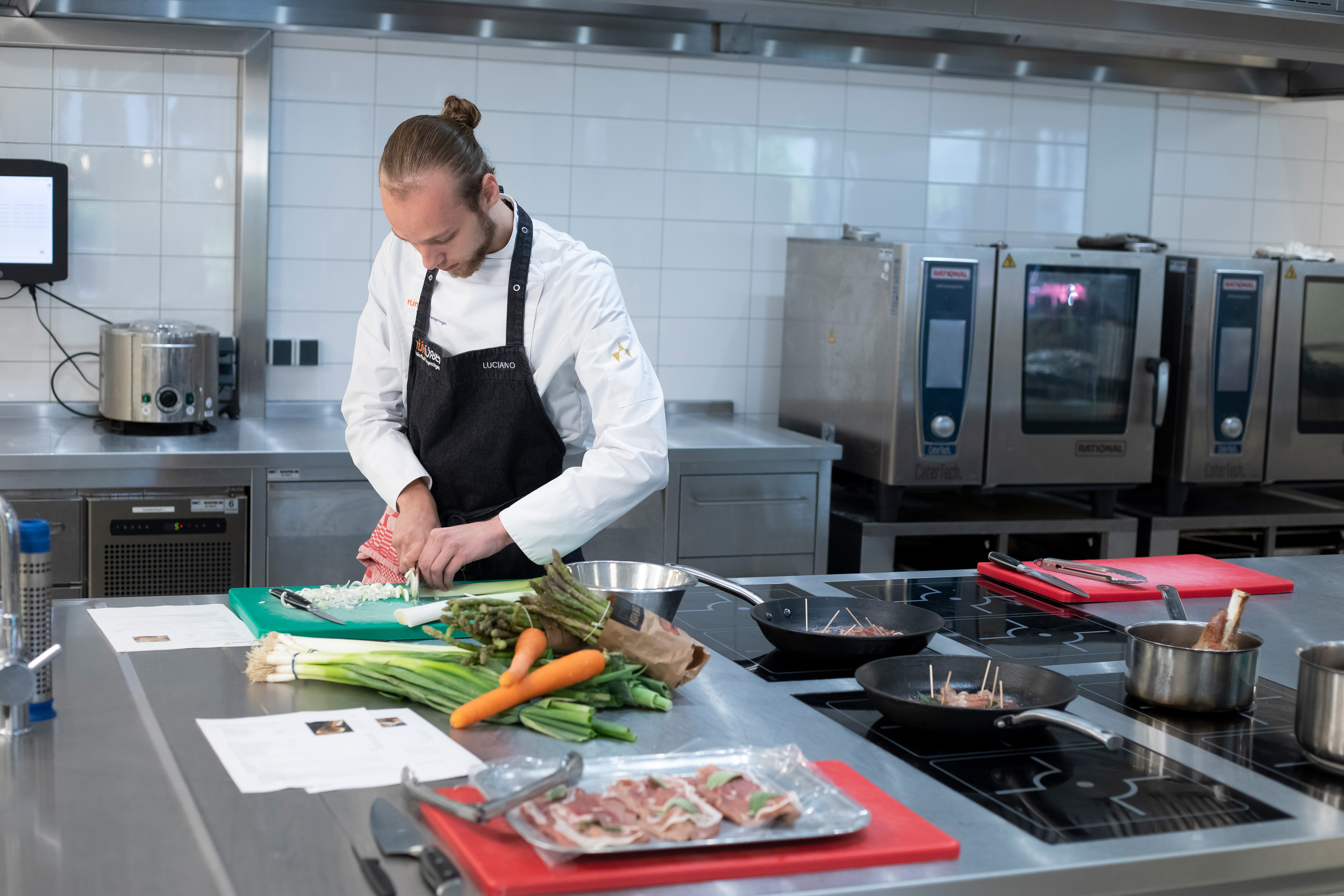 Jongen in kokskleding is een prei aan het snijden