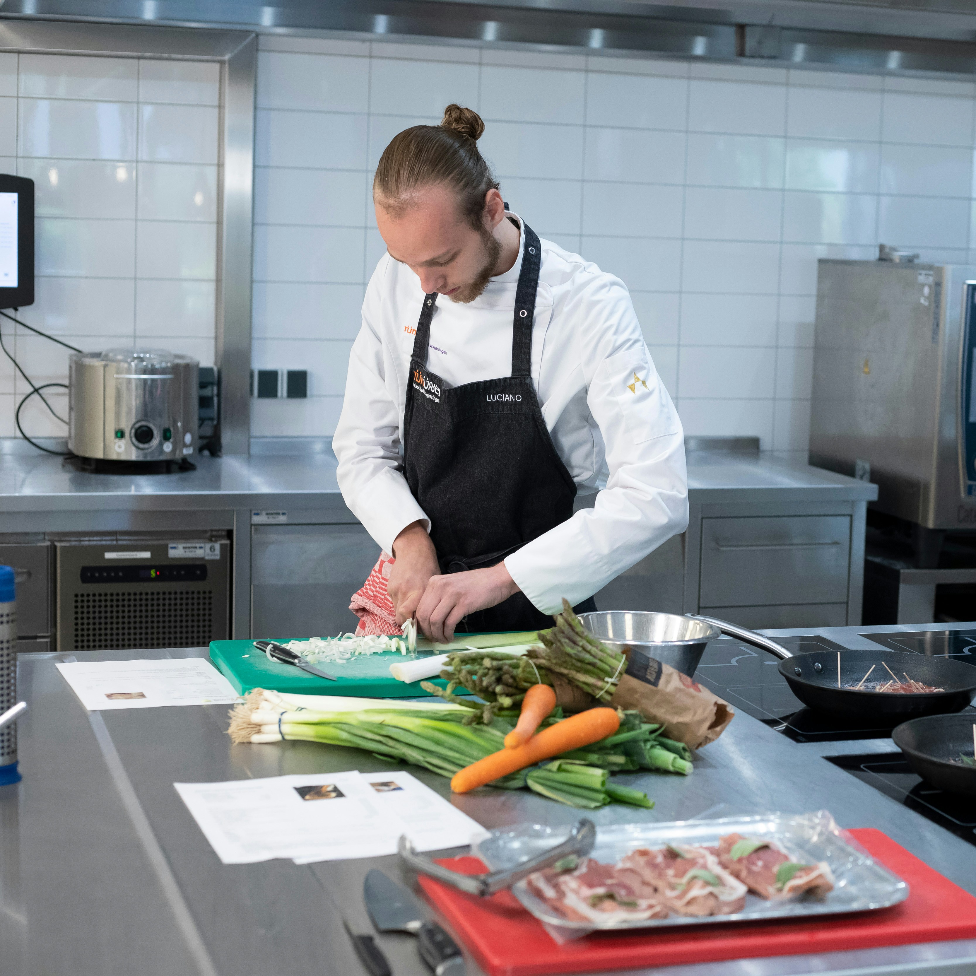 Jongen in kokskleding is een prei aan het snijden