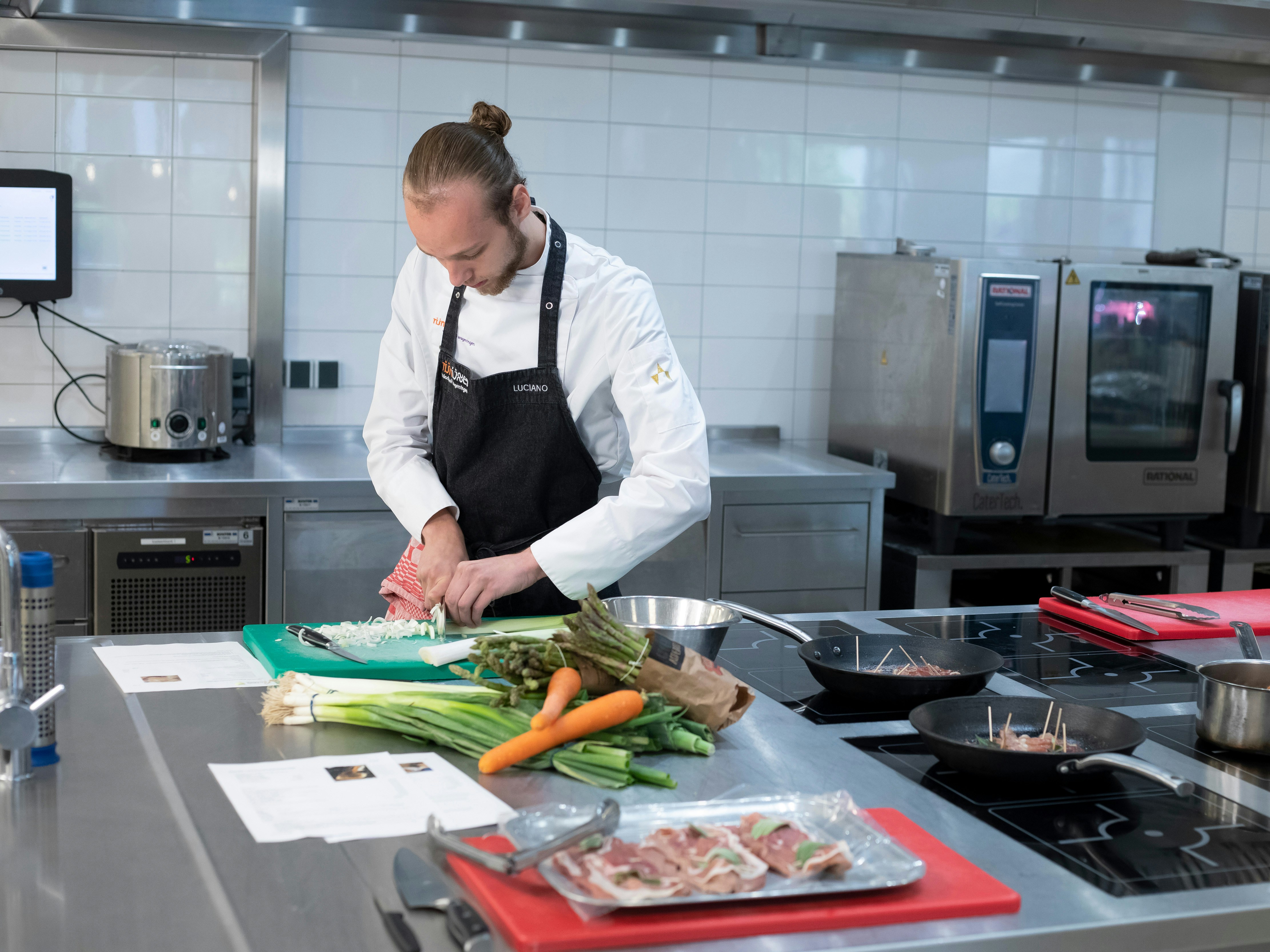 Jongen in kokskleding is een prei aan het snijden