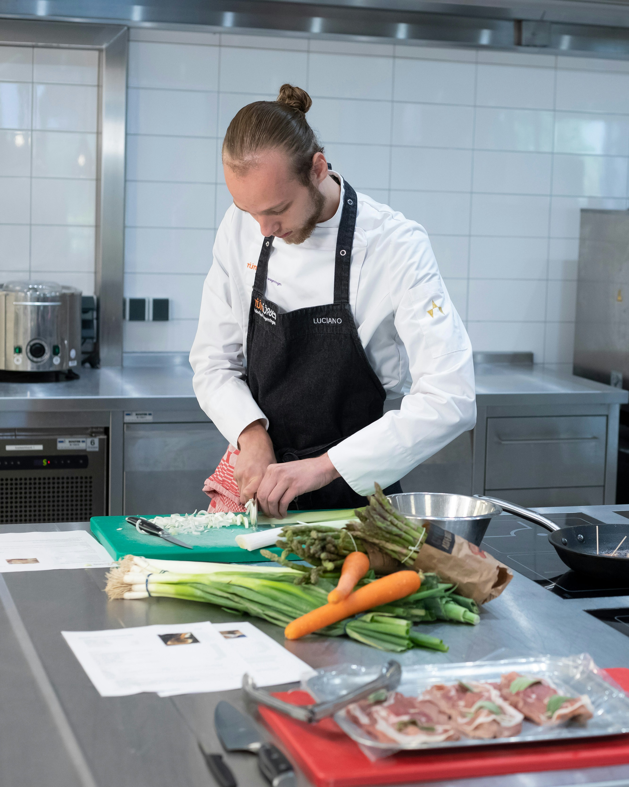 Jongen met kokskleding is een prei aan het snijden