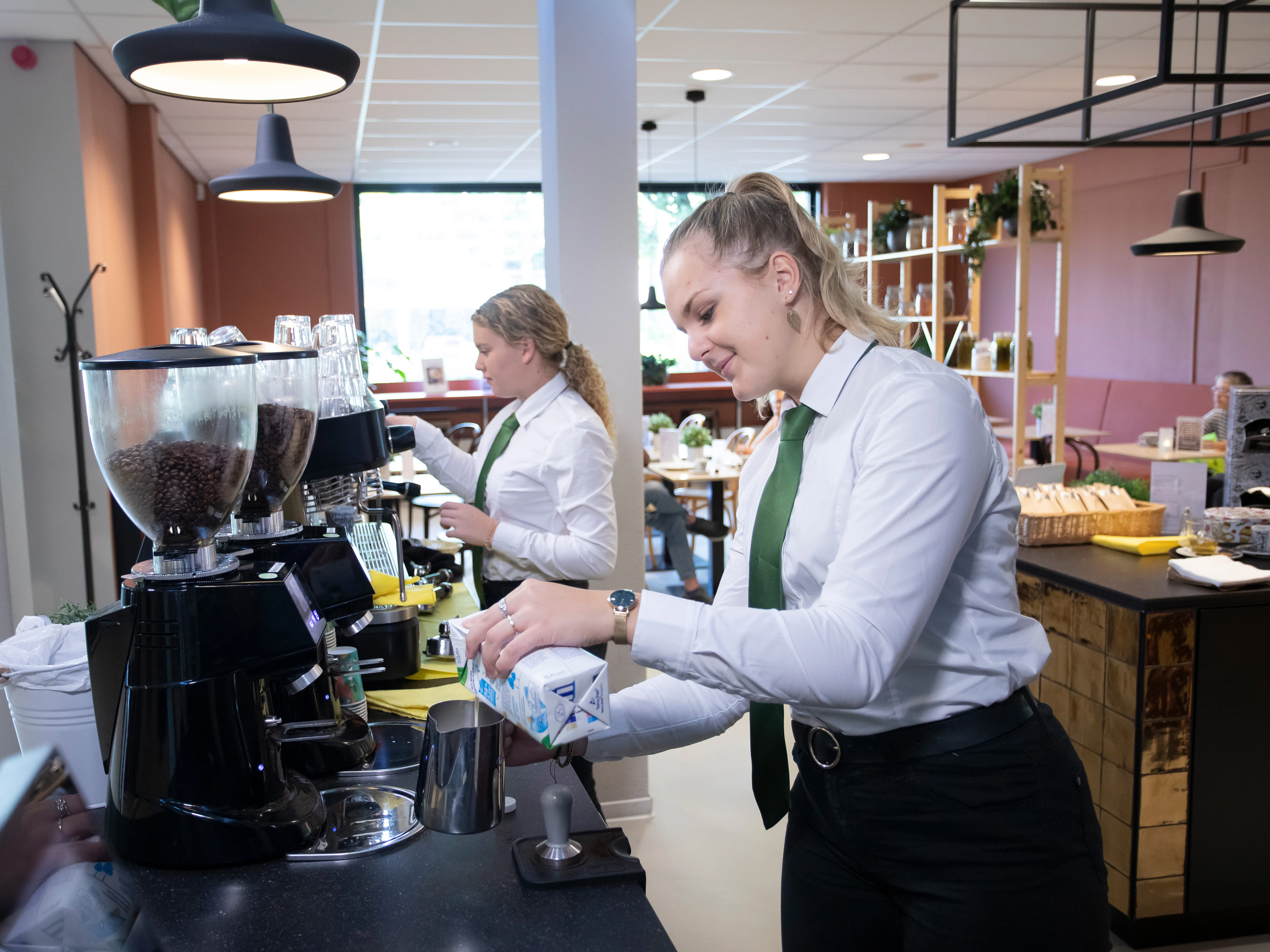 Meisje doet melk in de schuimer voor de cappucino