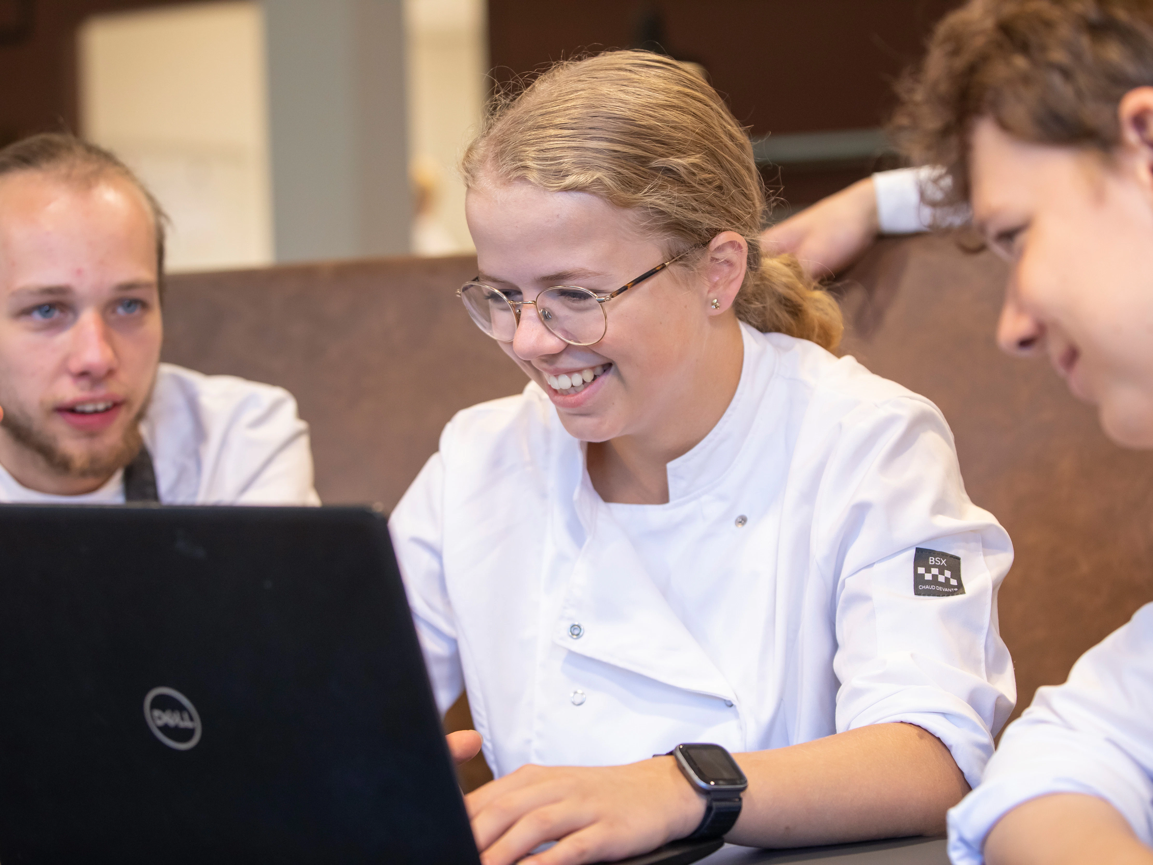3 studenten zitten aan tafel en kijken naar een laptopscherm