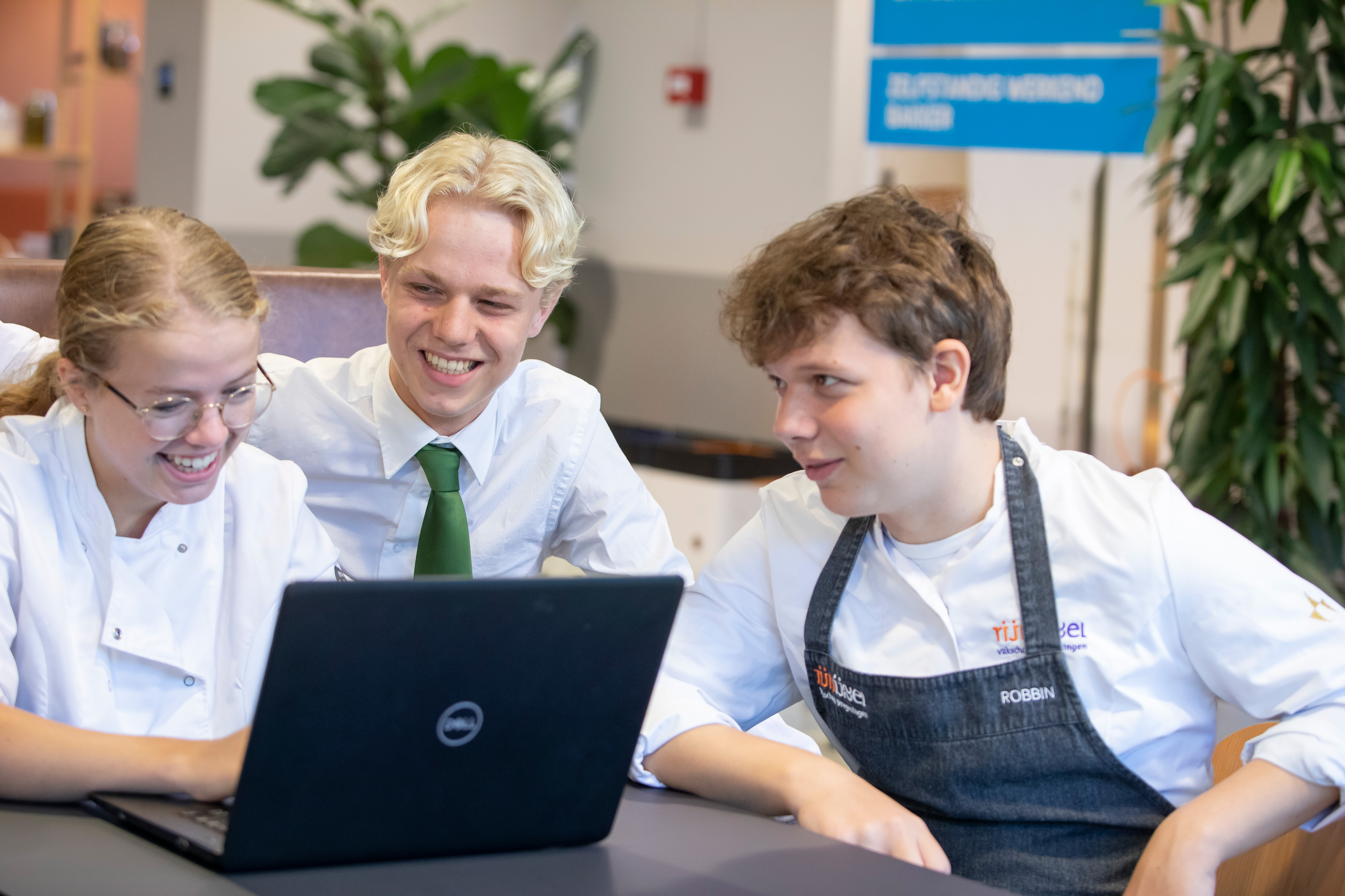 drie studenten zitten achter een laptop en kijken naar het scherm