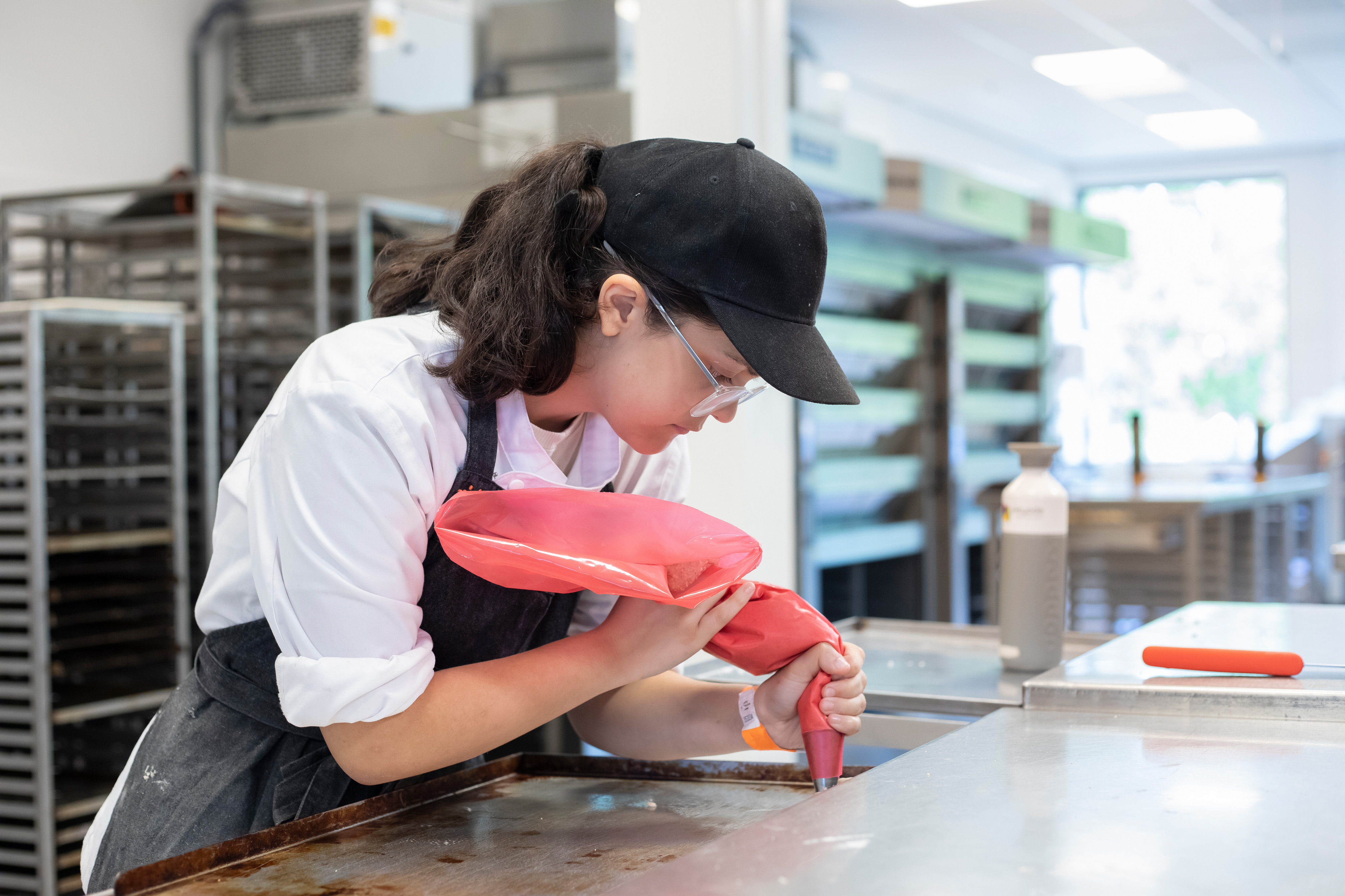 Meisje in bakkerskleding is bezig met het opspuiten van Macarons op een bakplaat. In de bakkerij.