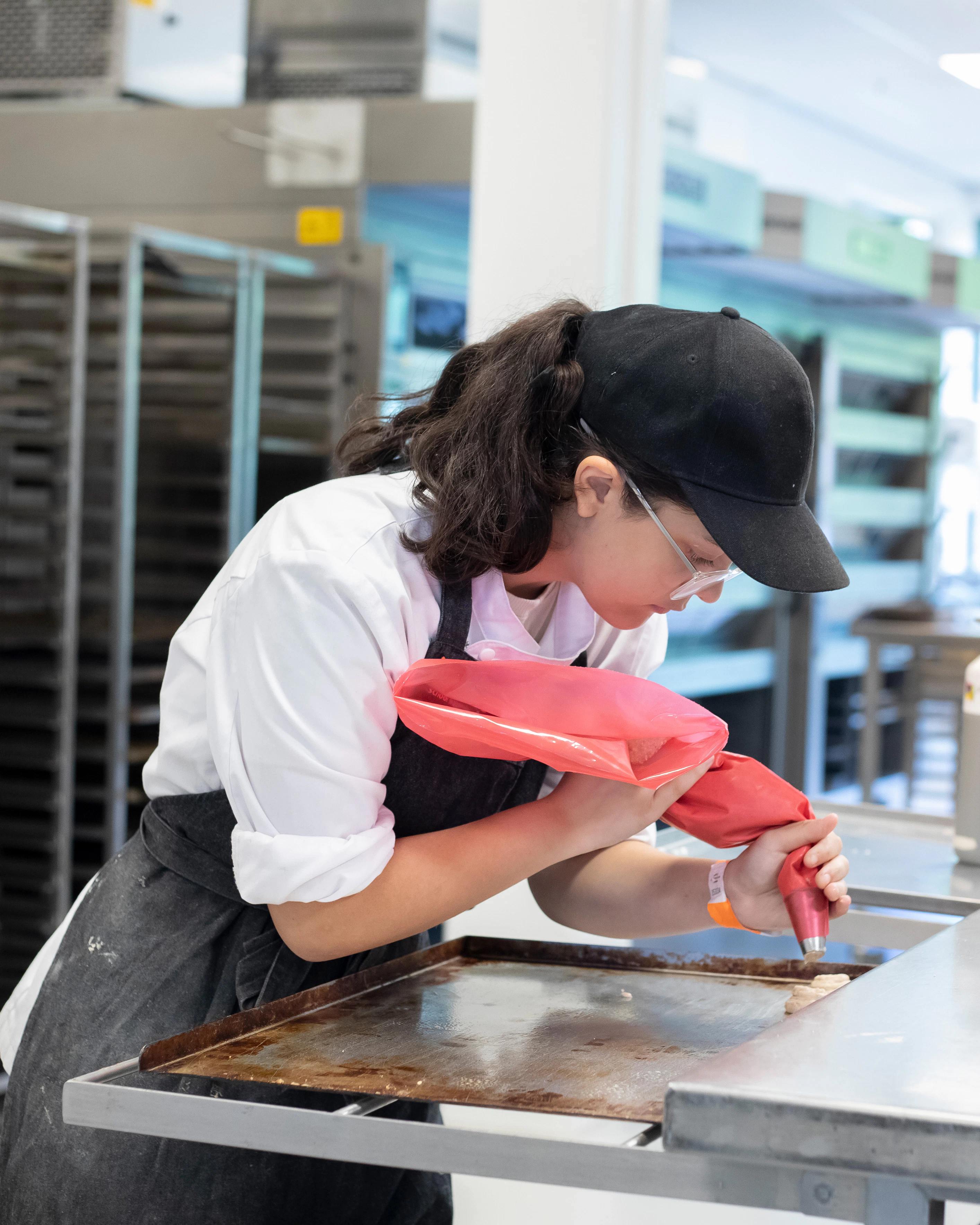 Een meisje in bakkerskleding is bezig met een spuitzak om lekkernijen te maken