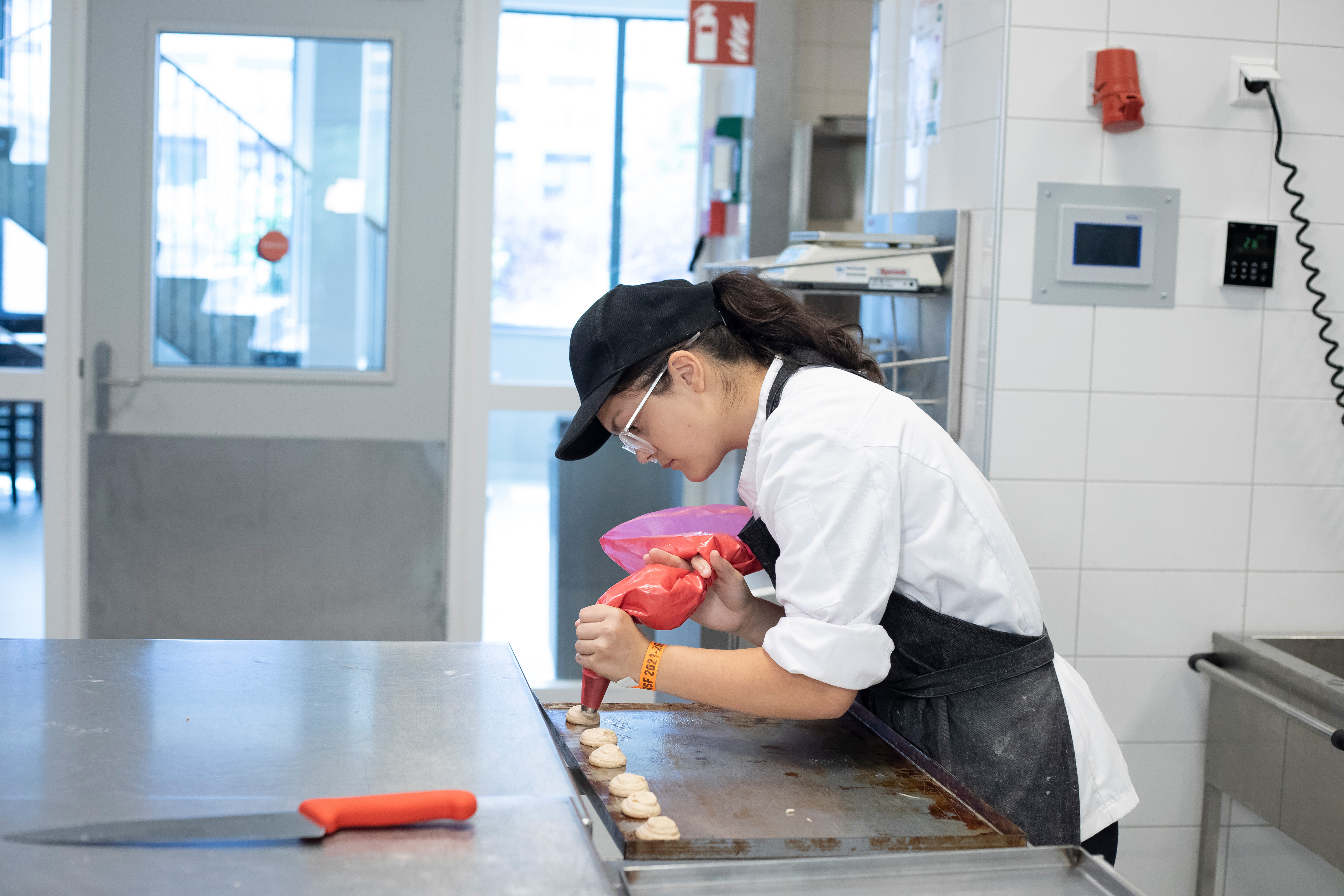 Een meisje in bakkerskleding is bezig met een spuitzak om lekkernijen te maken