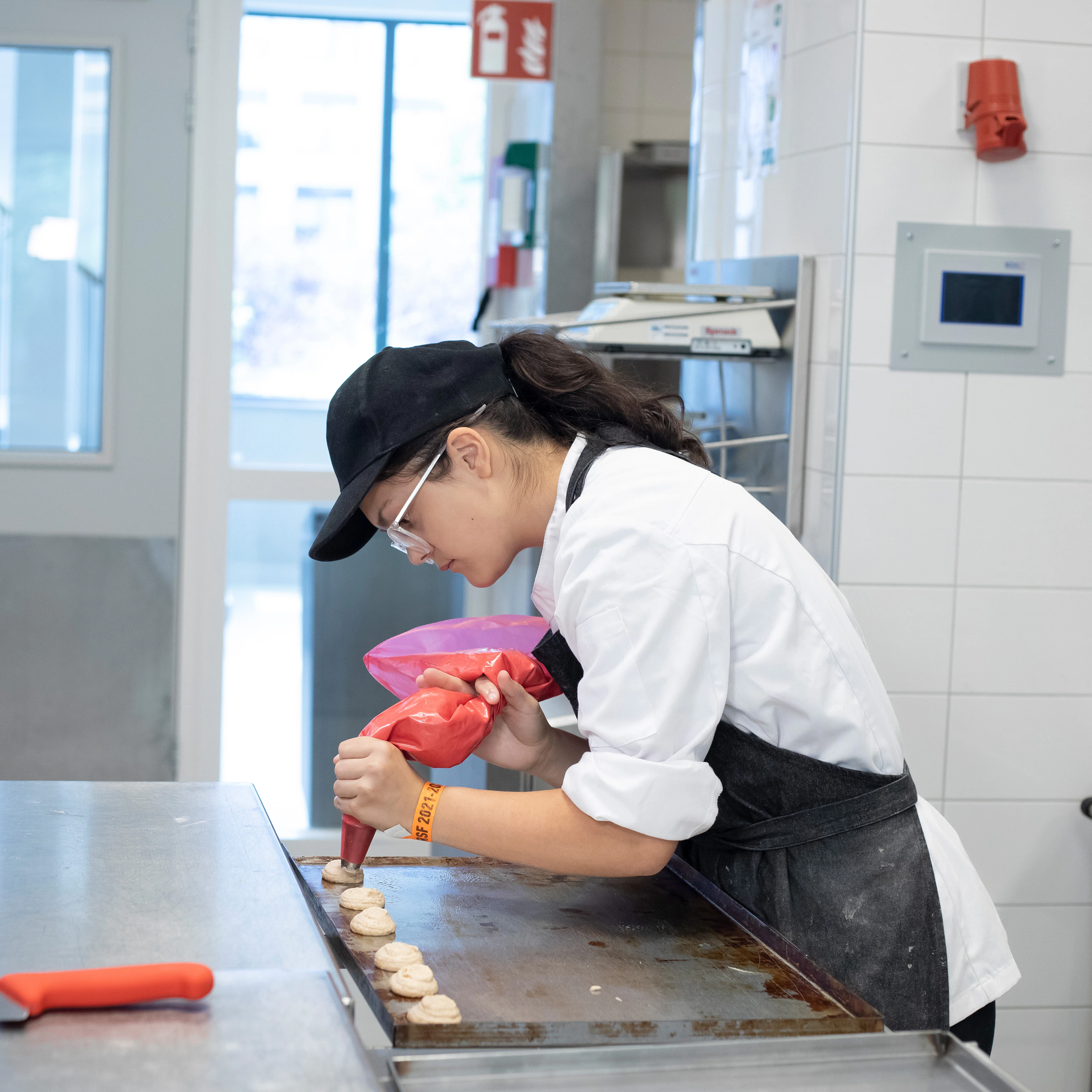 Een meisje in bakkerskleding is bezig met een spuitzak om lekkernijen te maken