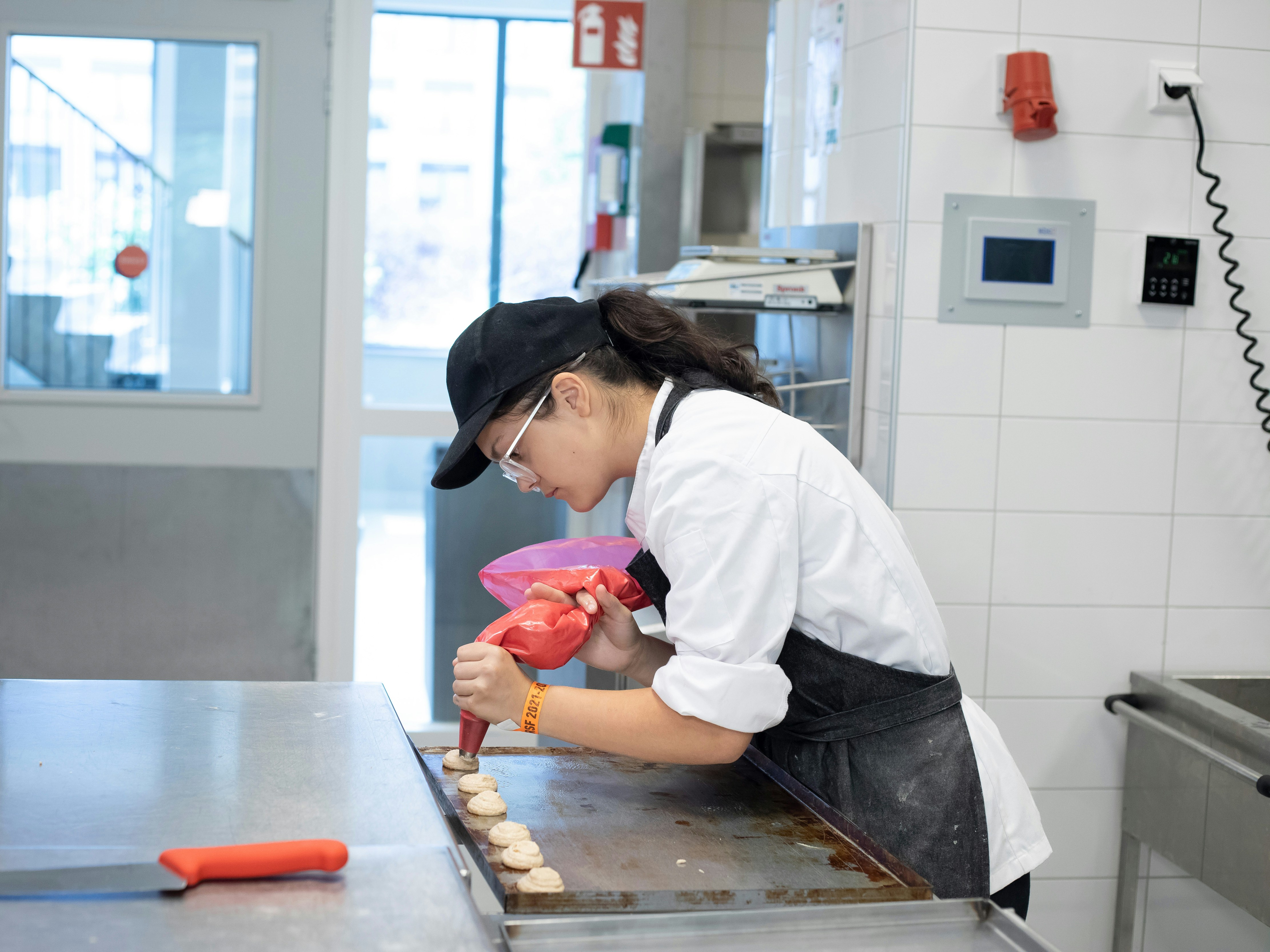 Een meisje in bakkerskleding is bezig met een spuitzak om lekkernijen te maken