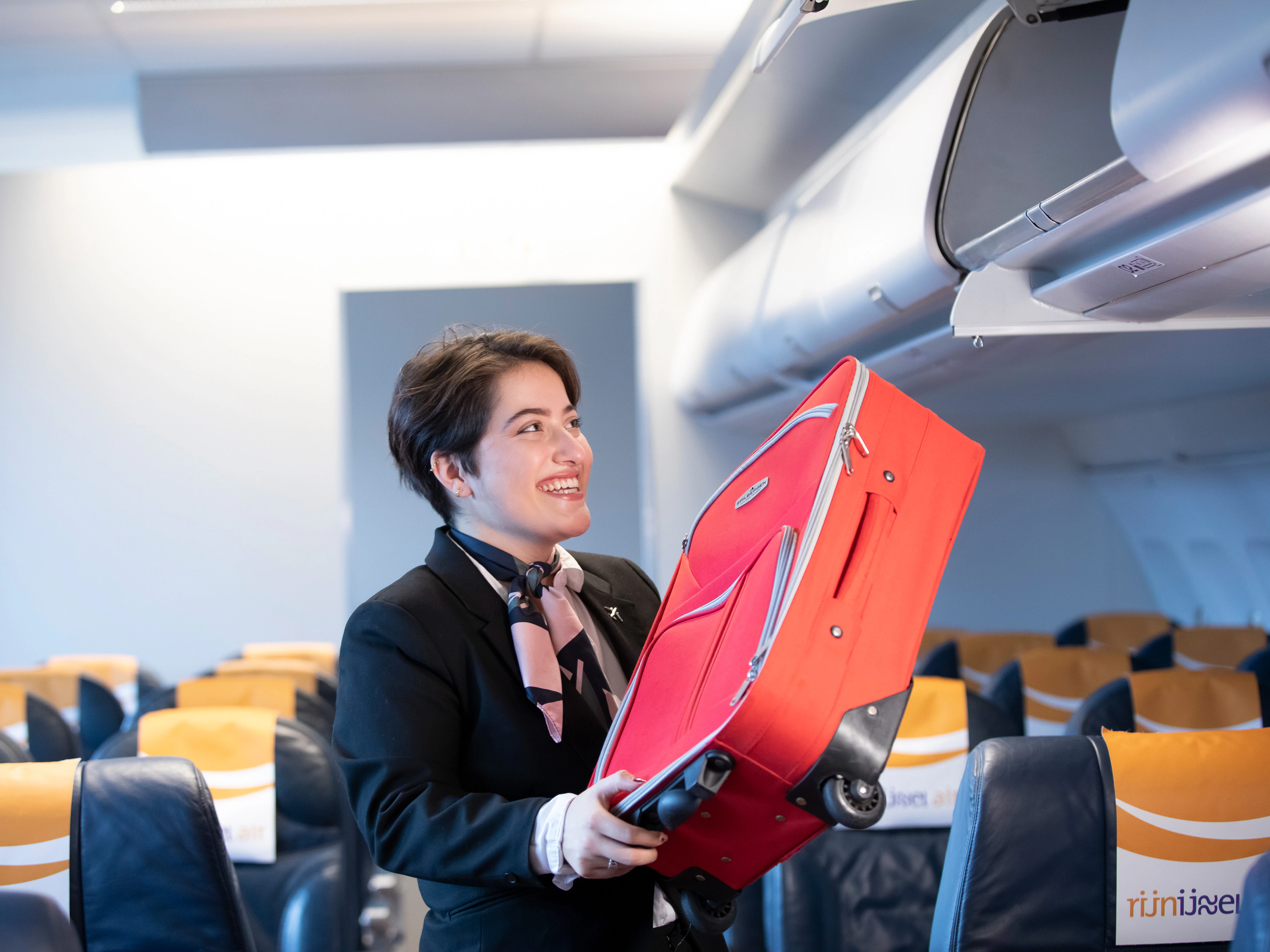 Student doet een koffer in het opbergbak van een vliegtuig