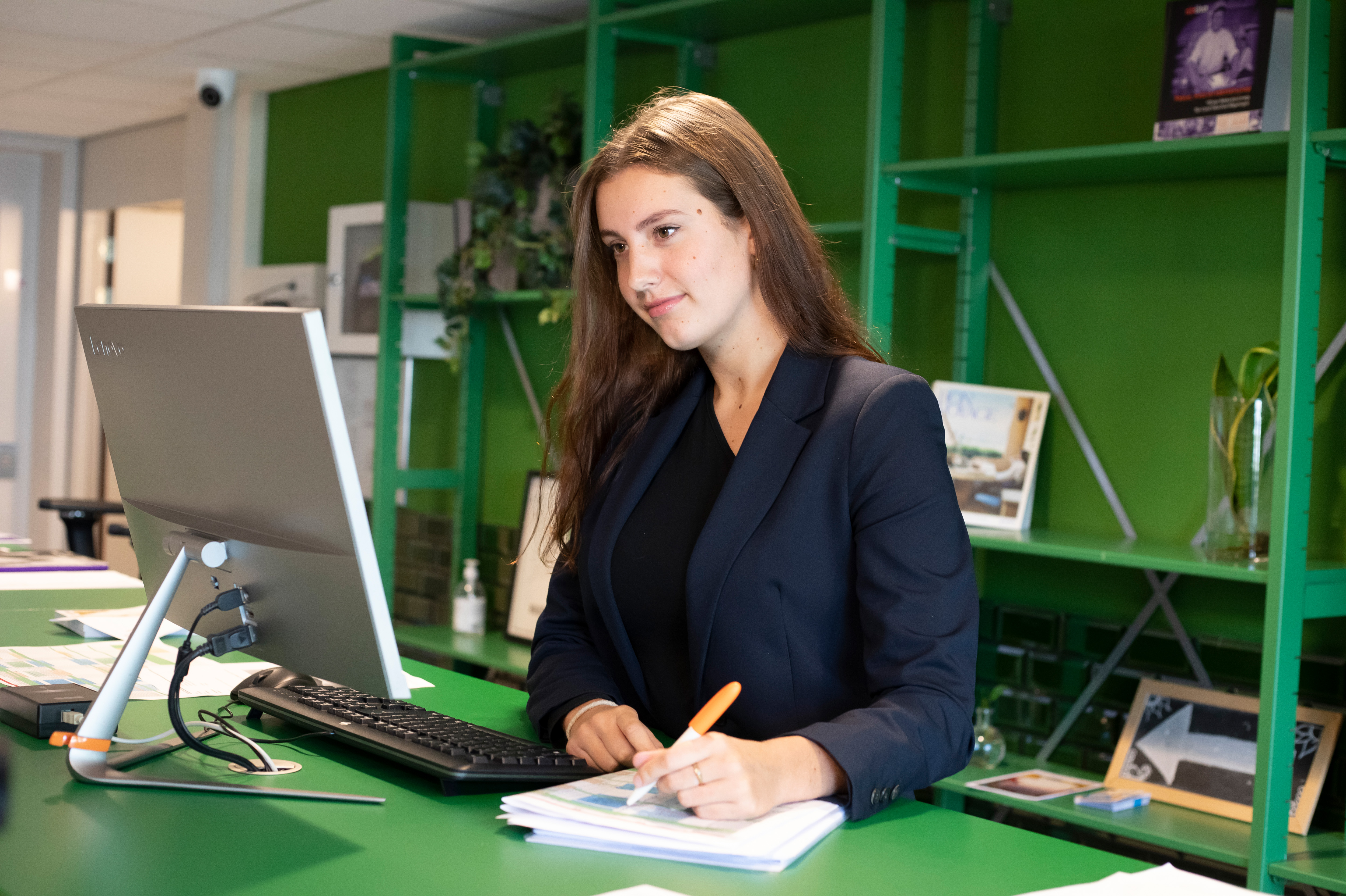 Een meisje staat achter een computer. Terwijl ze naar het scherm kijkt, is ze ook iets aan het opschrijven