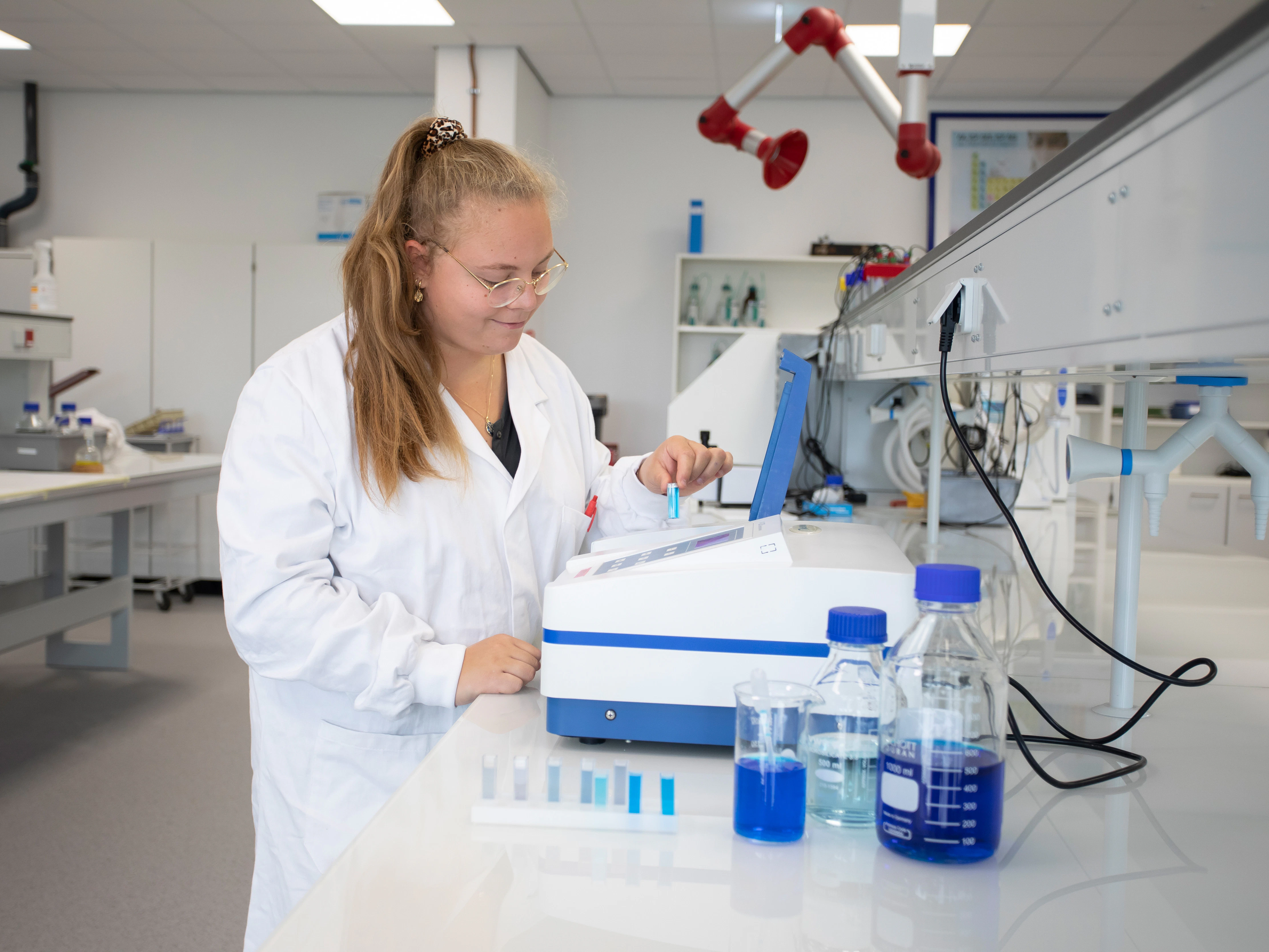 Meisje in een witte labaratoriumjas is bezig met blauwe chemische vloeistoffen in buisjes