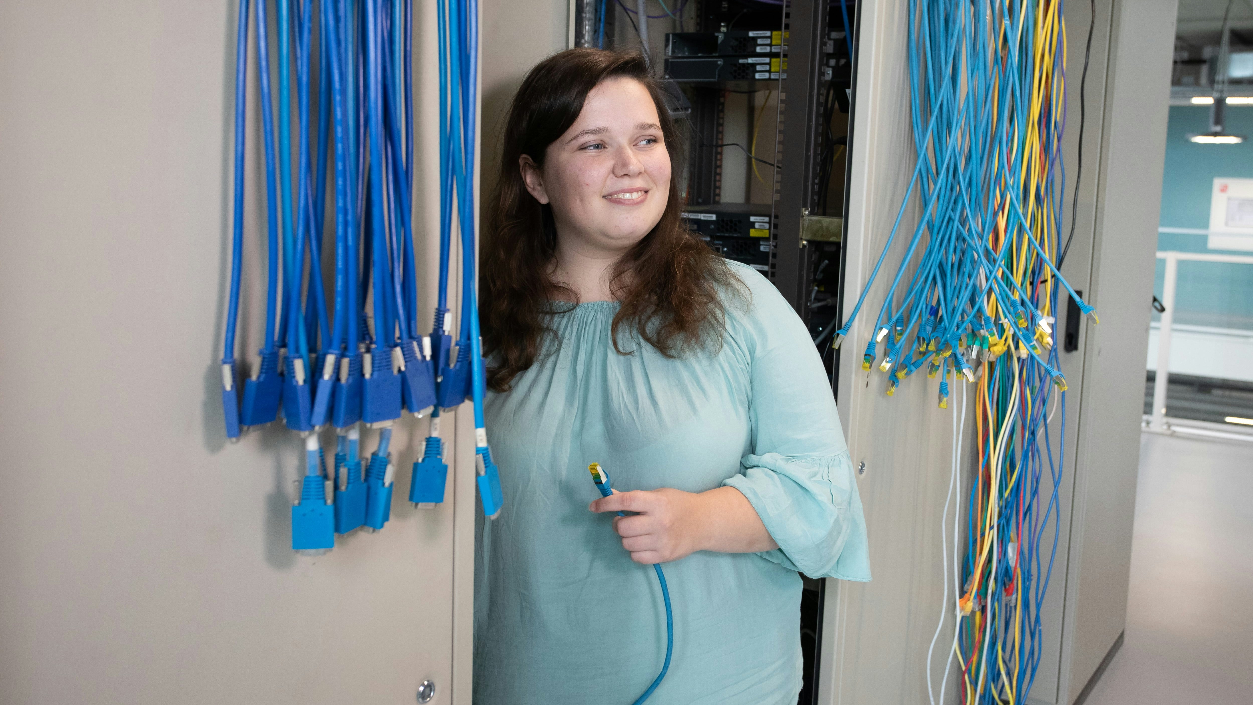 Student staat in een kast met allemaal kabels en heeft een kabel in de hand
