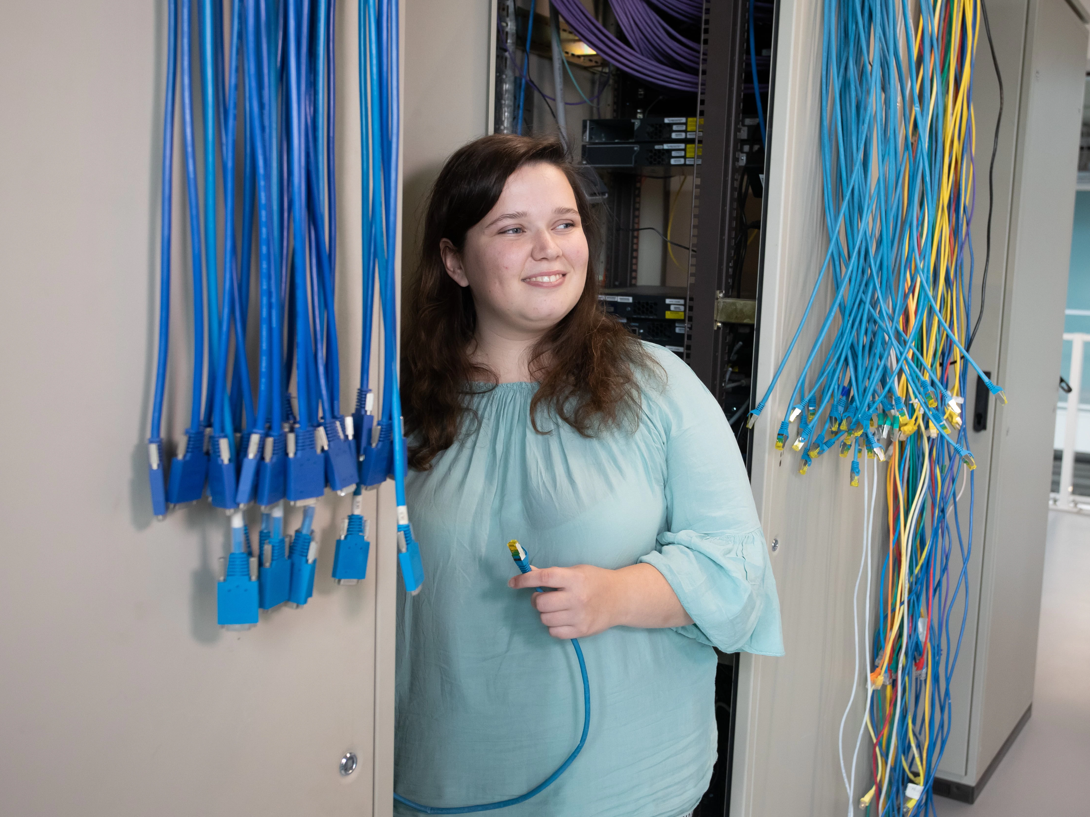 Student staat in een kast met ICT apparatuur en kabels