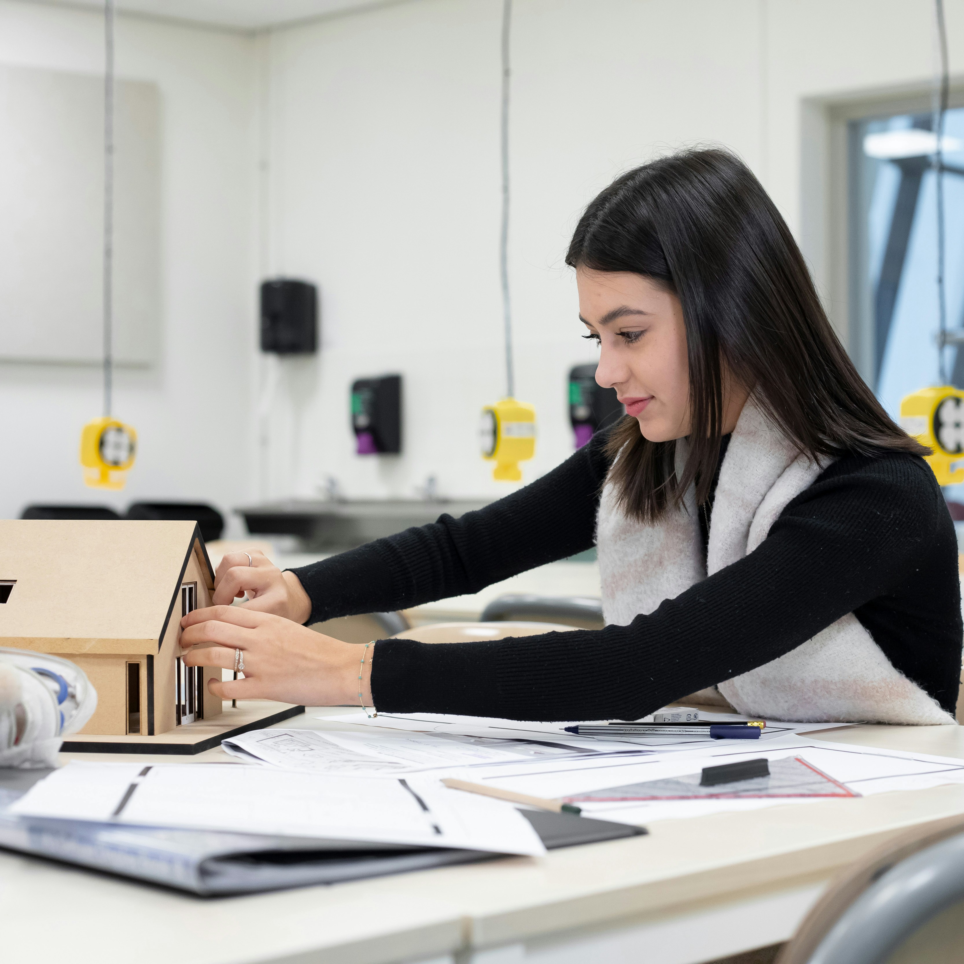Meisje is bezig met een maquette terwijl op de tafel pennen en papier liggen