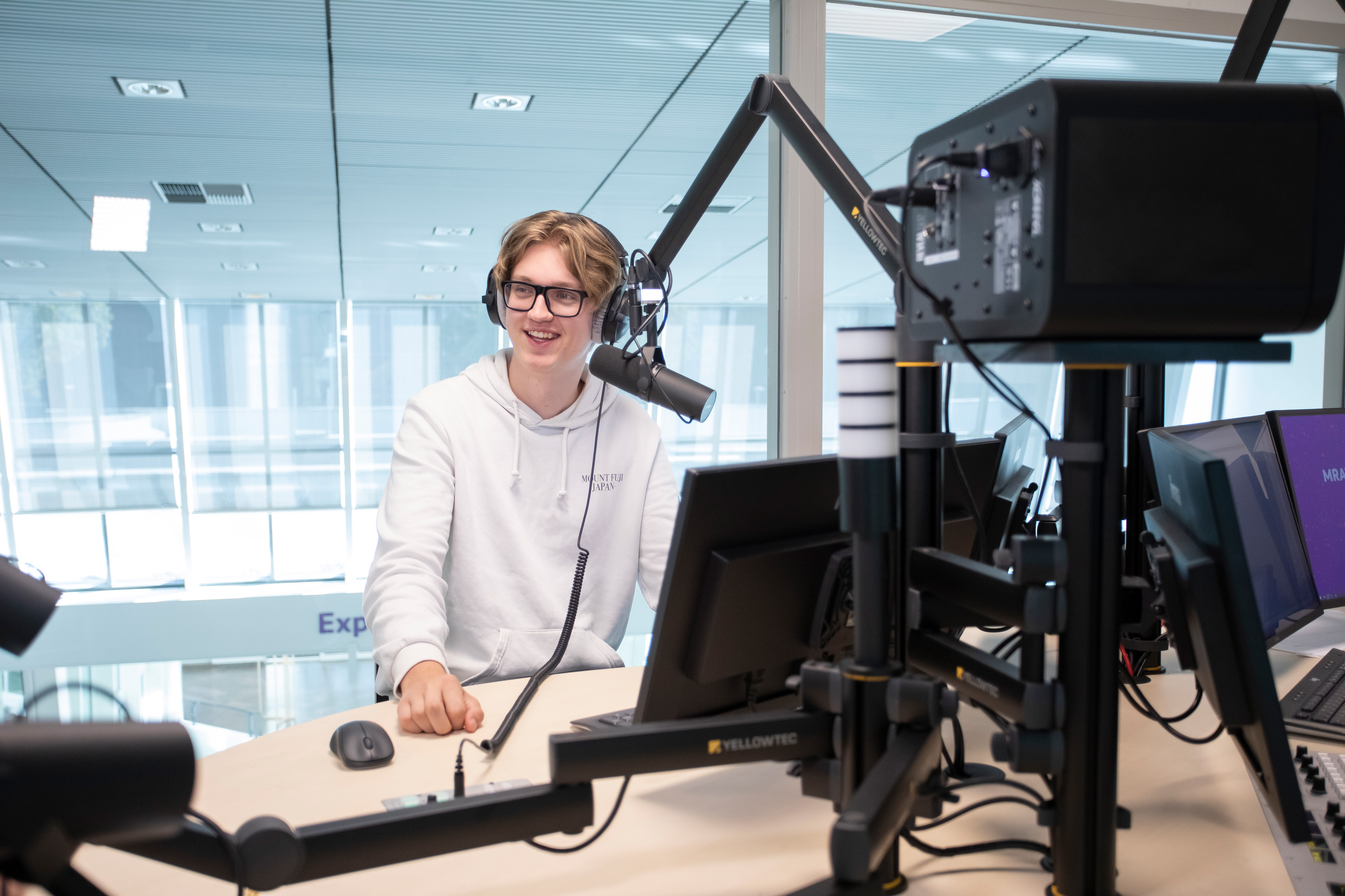 Student zit in een radiostudio achter een microfoon met een koptelefoon op