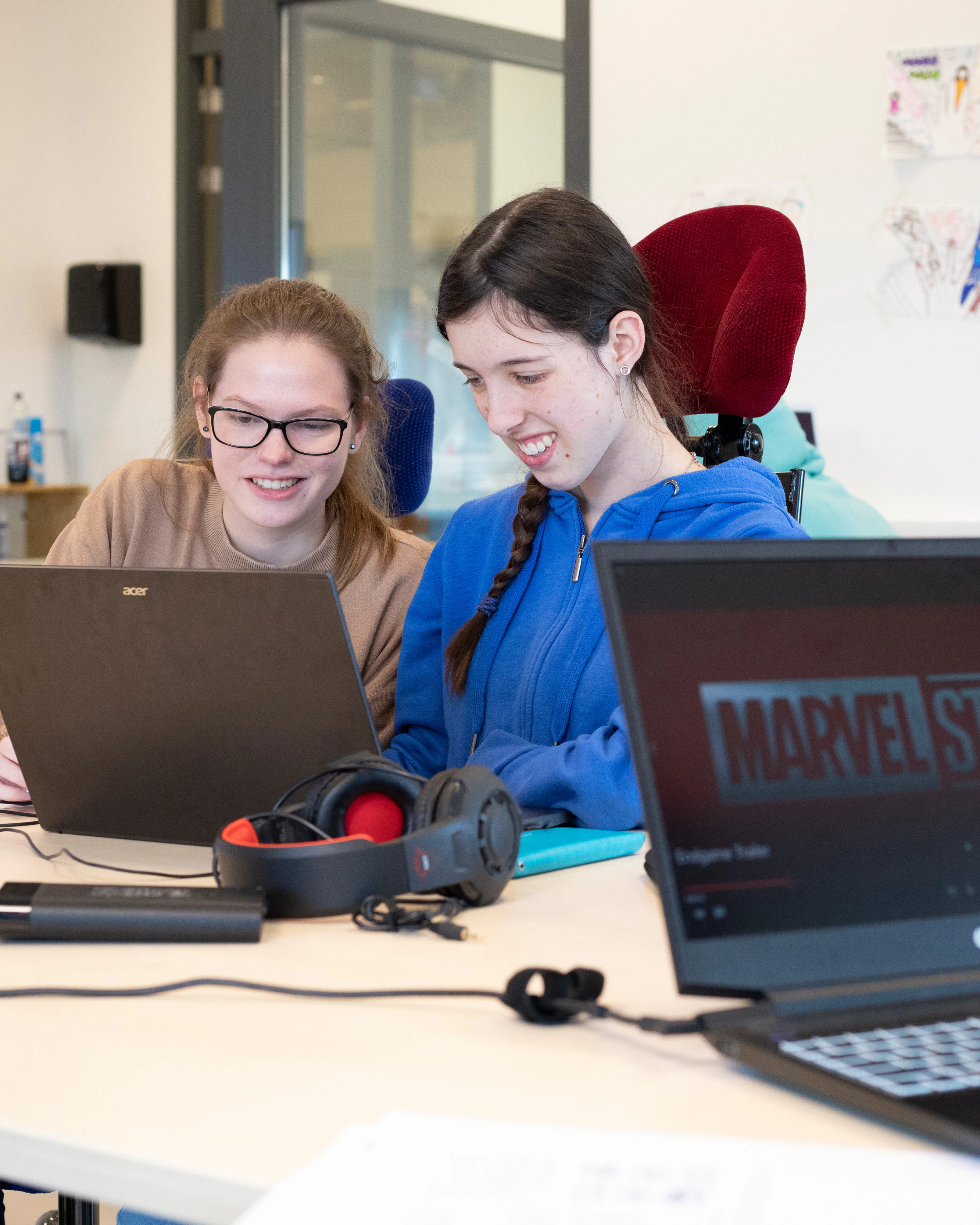 twee studenten kijken naar een laptopscherm. Er ligt ook een koptelefoon op tafel
