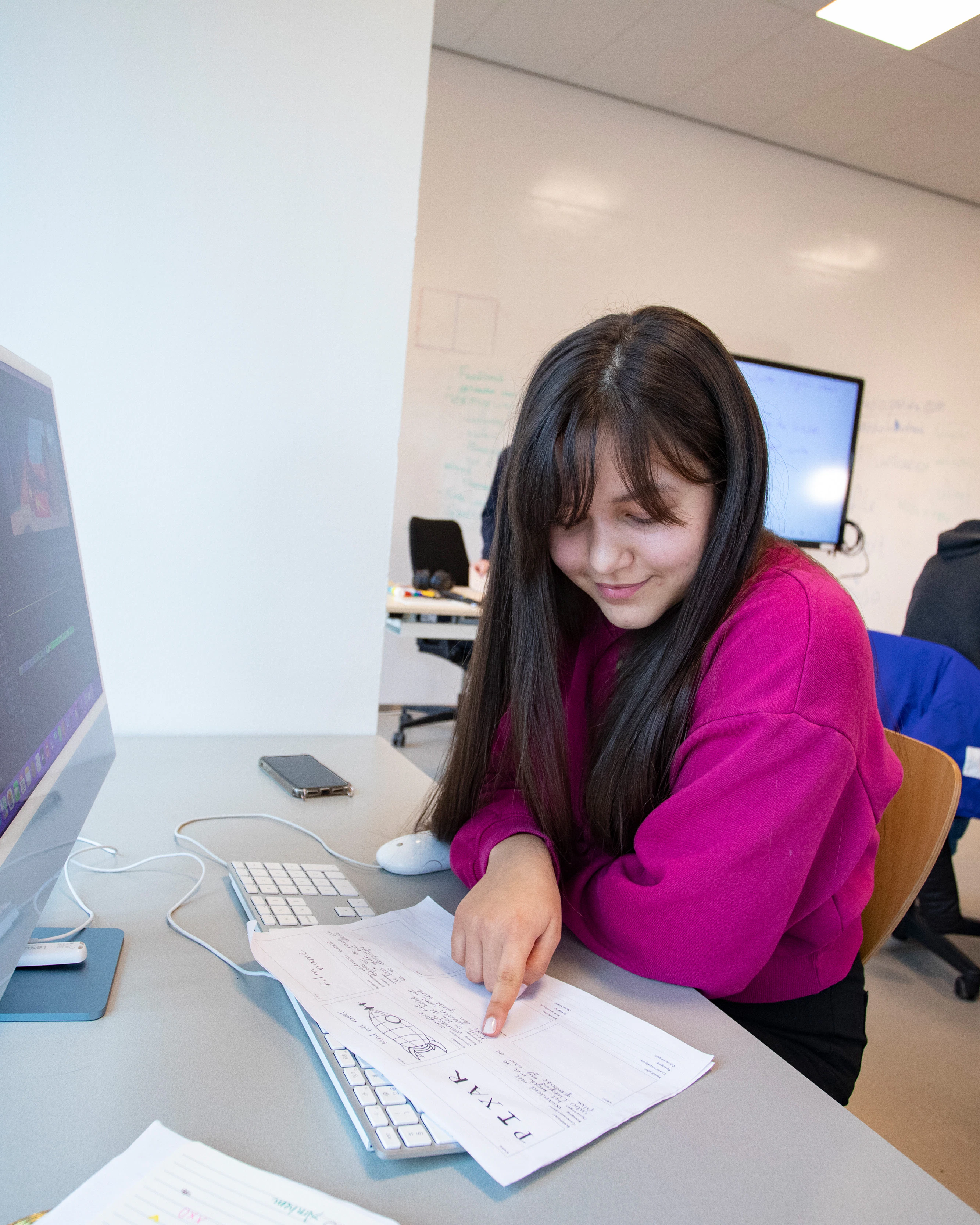 Student zit achter een computer en wijst met haar vinger op een blaadje