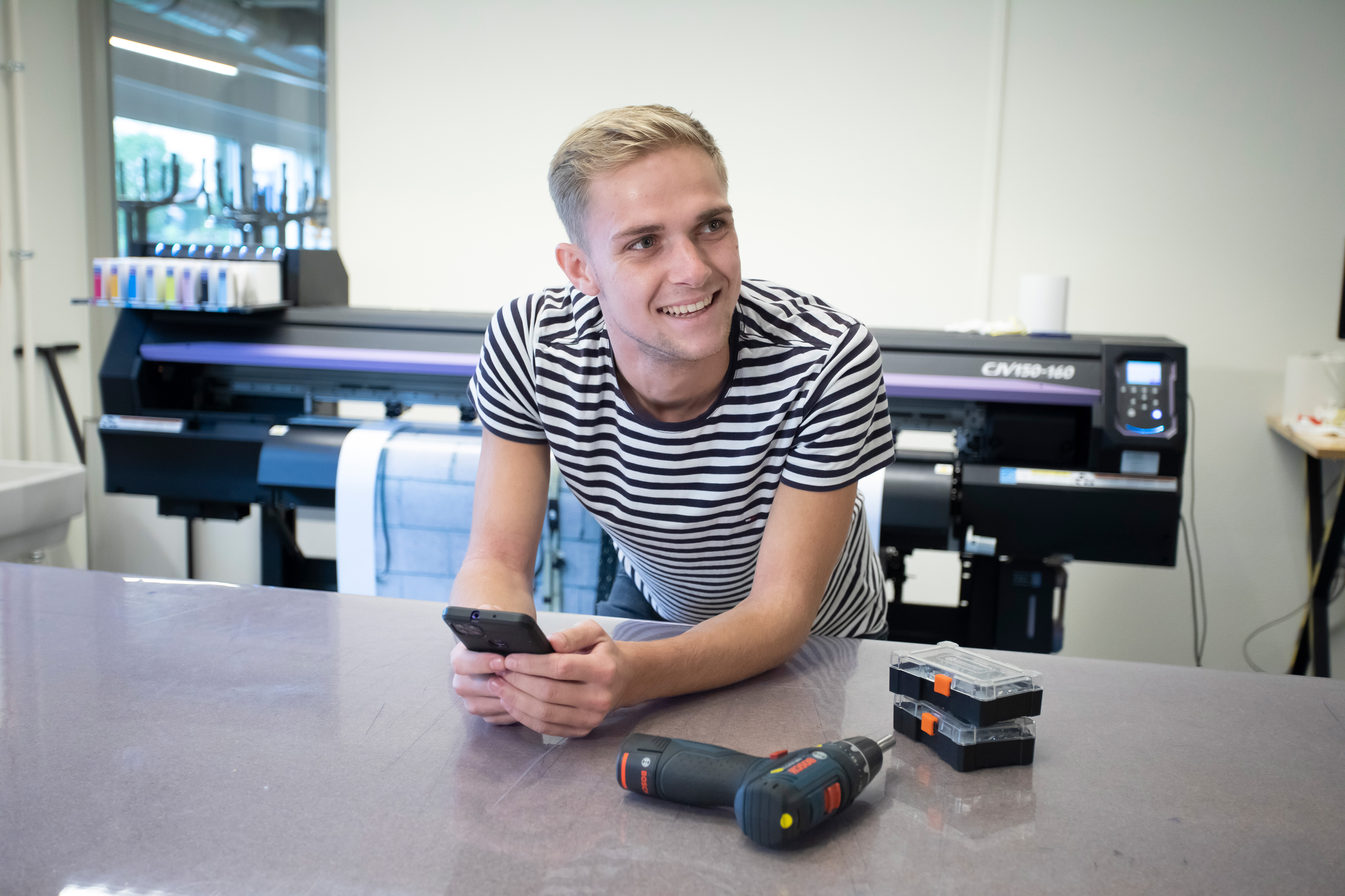Student leunt op een tafelblad met een telefoon in de hand