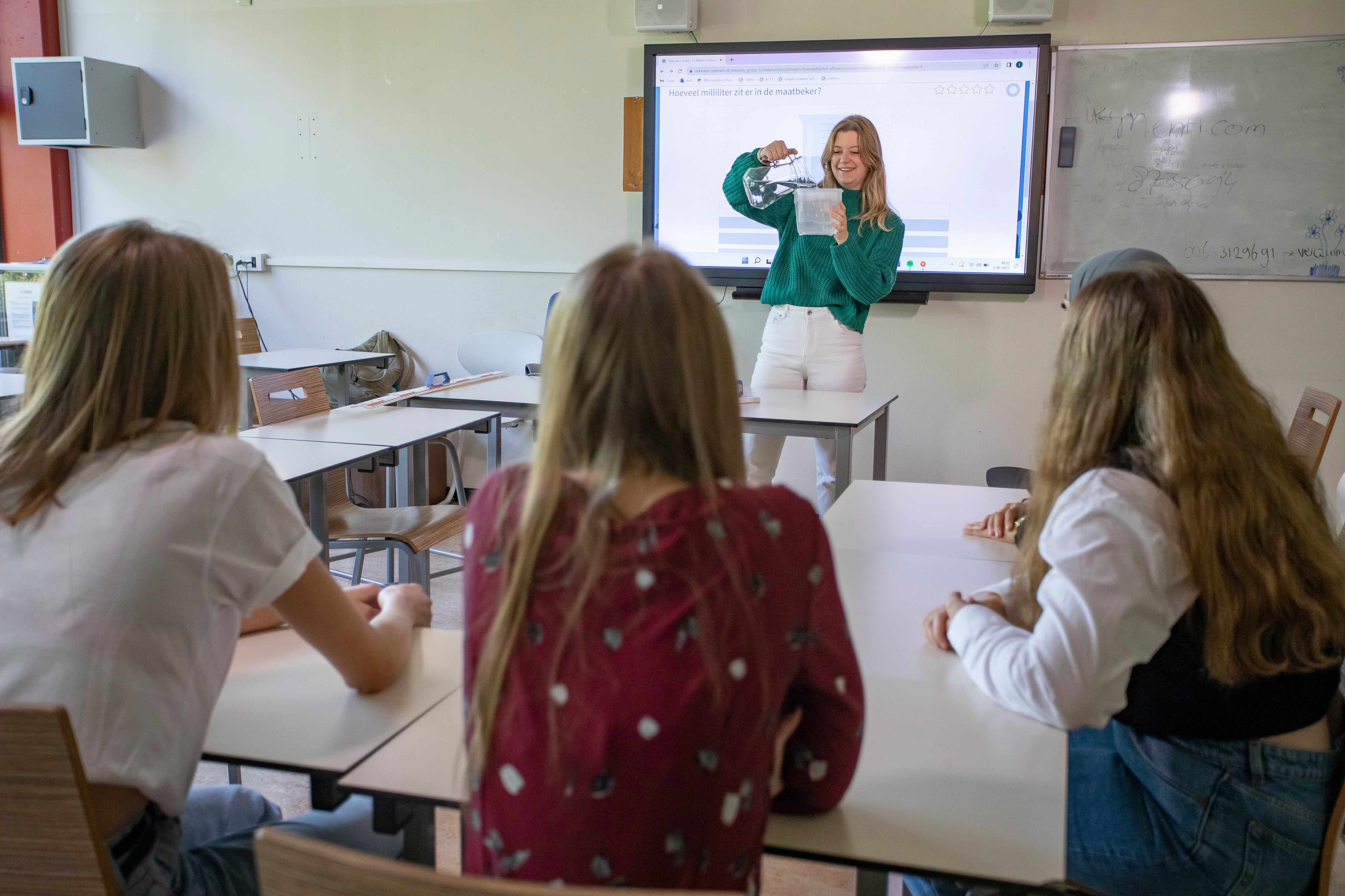 Student staat voor de klas met een maatbeker