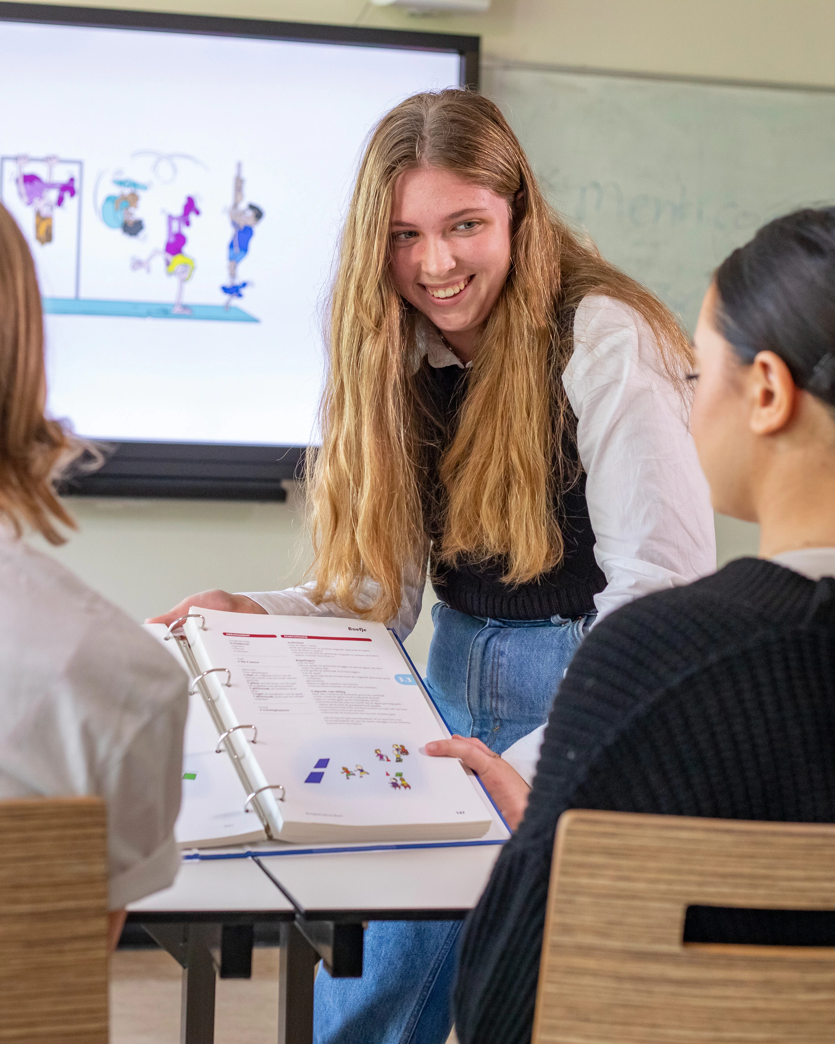 Student wijst op een boek terwijl ze voor 2 studenten zit