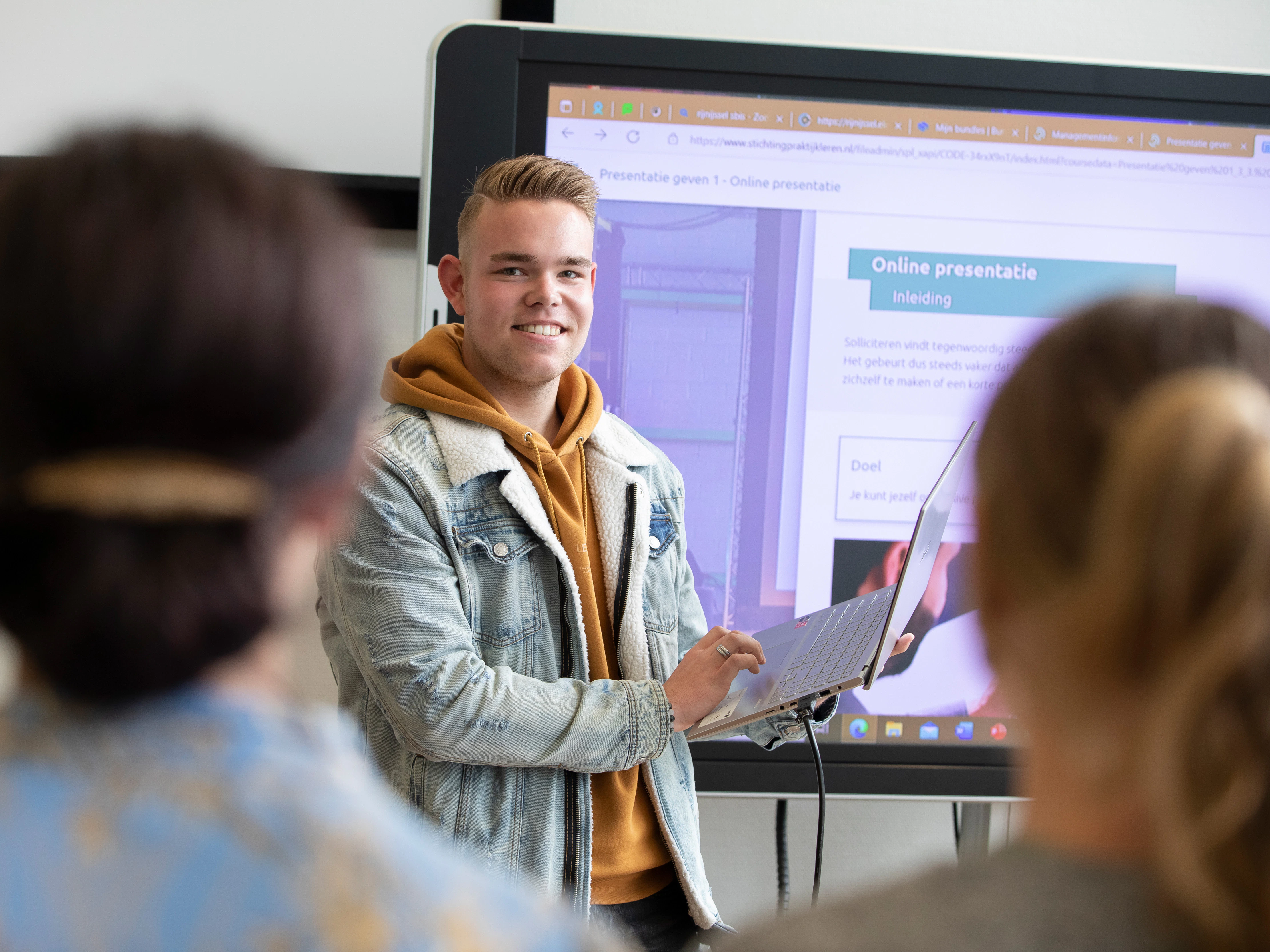 Student staat voor de klas en heeft een laptop in zijn hand