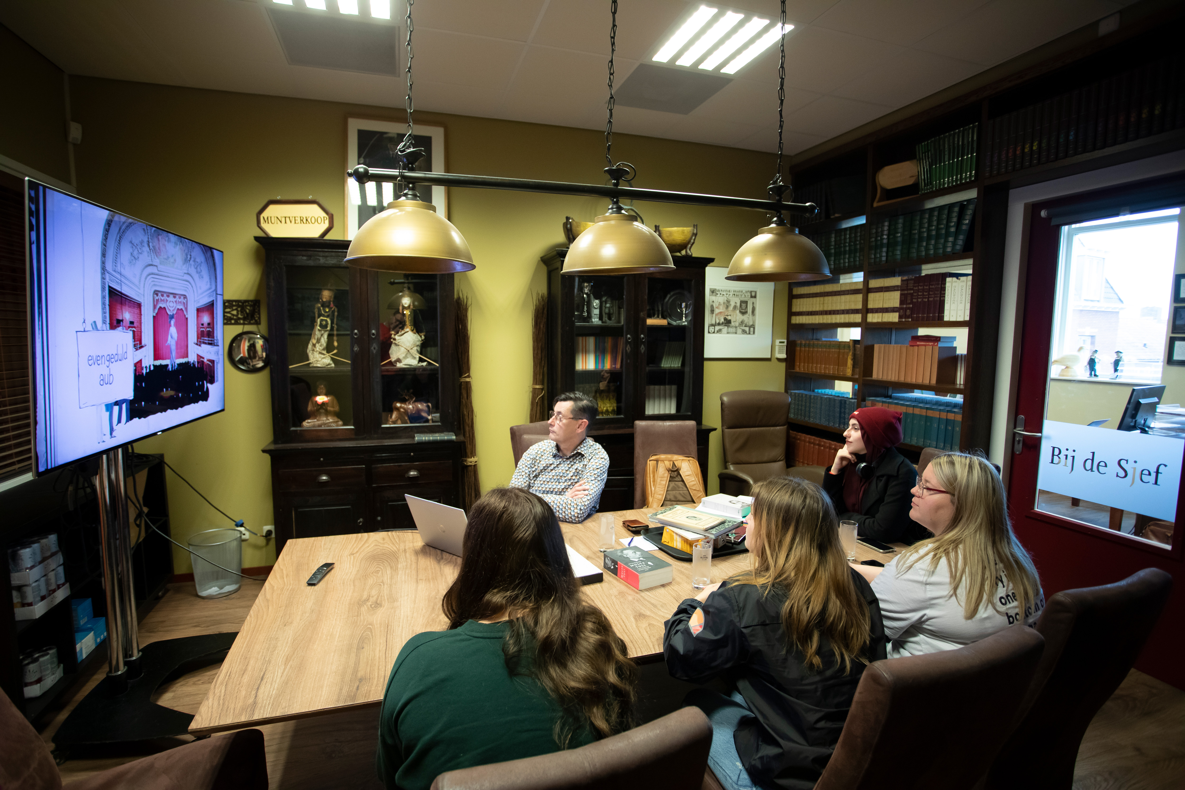 Studenten zitten aan tafel en kijken naar een groot scherm
