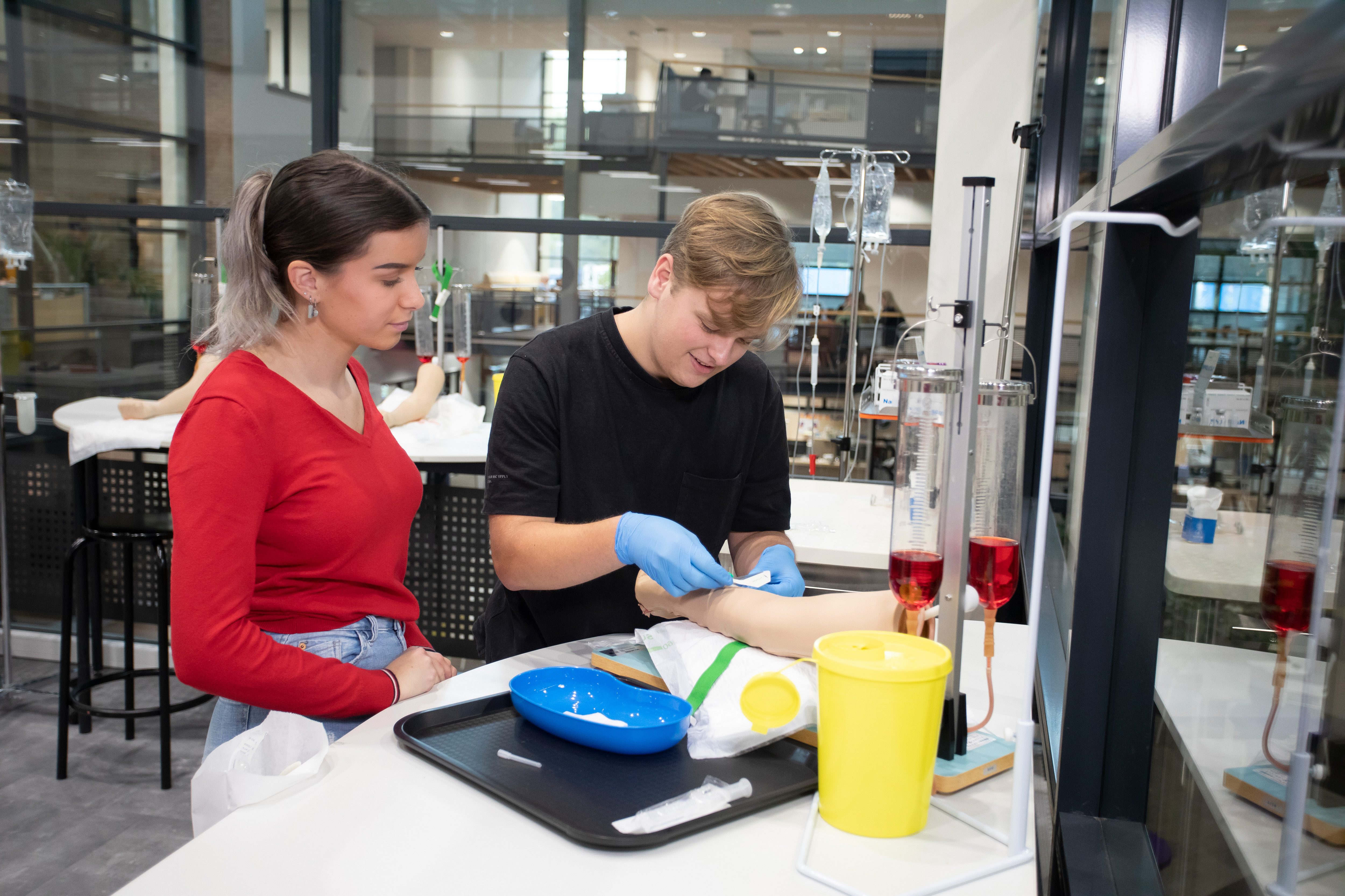 Student plakt een pleister op een been terwijl een student toekijkt