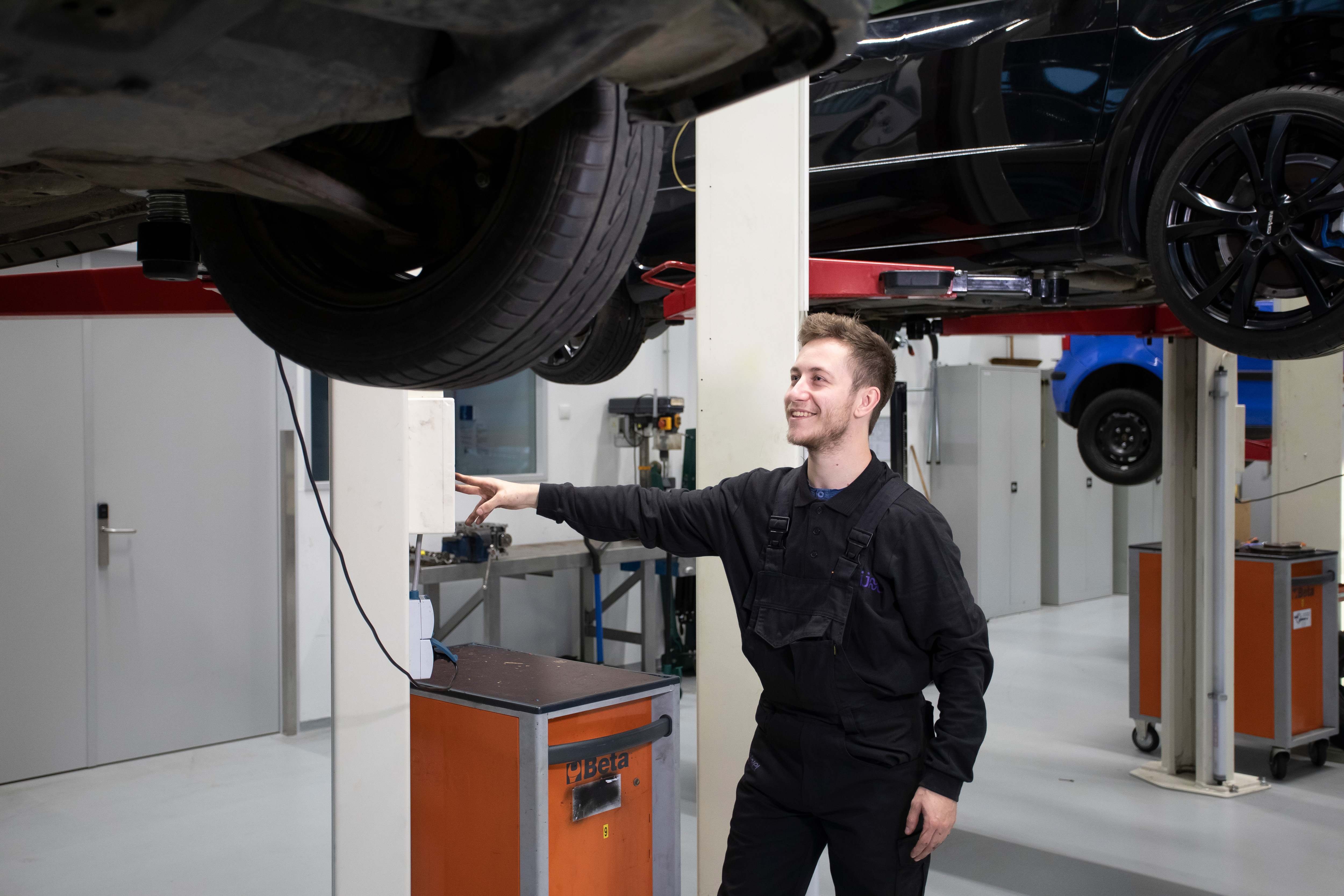 Student in werkkleding bestuurt de lift die een auto omhoog zet zodat de student er onder kan kijken