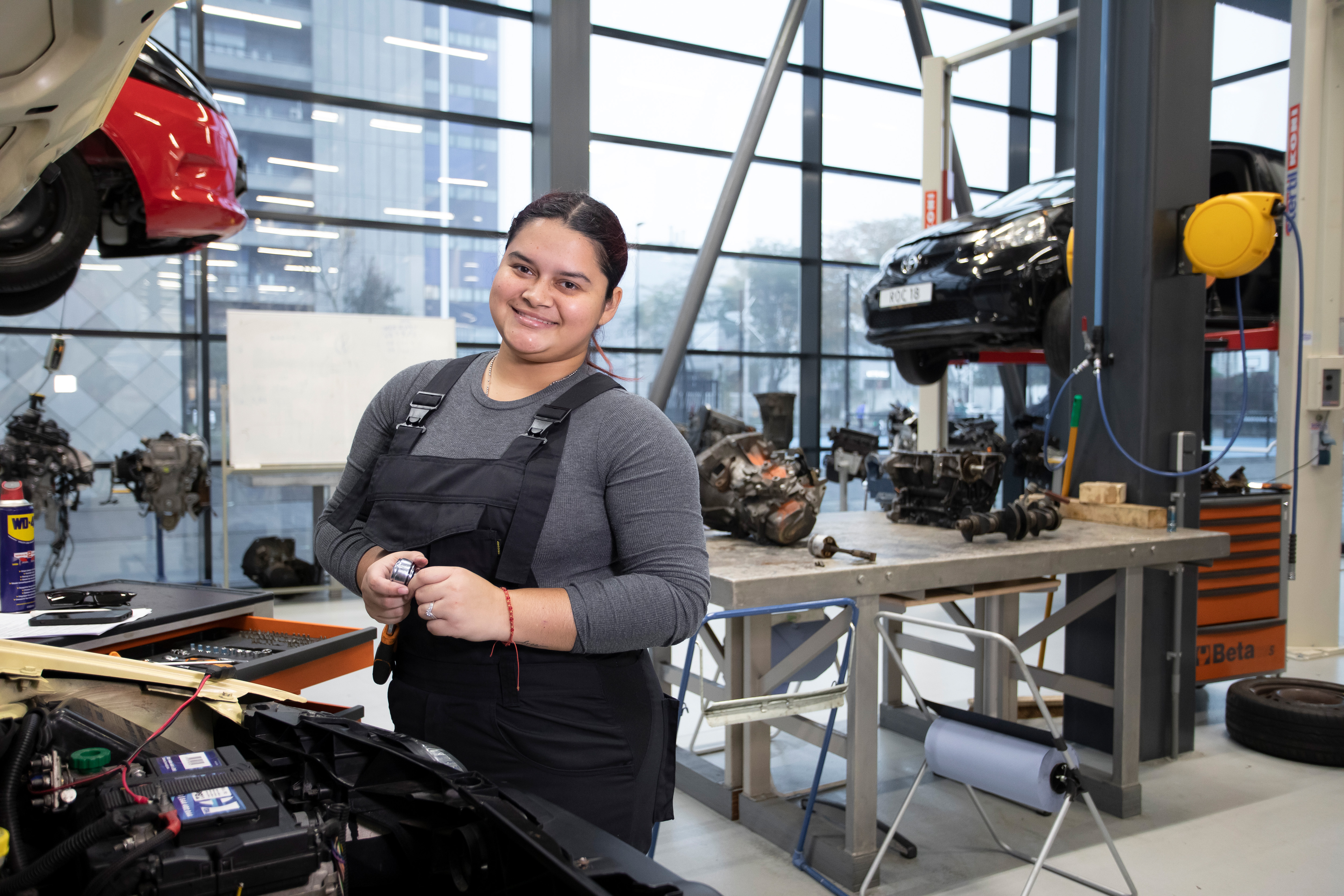 Student in werkkleding staat voor een auto met de motorkap omhoog