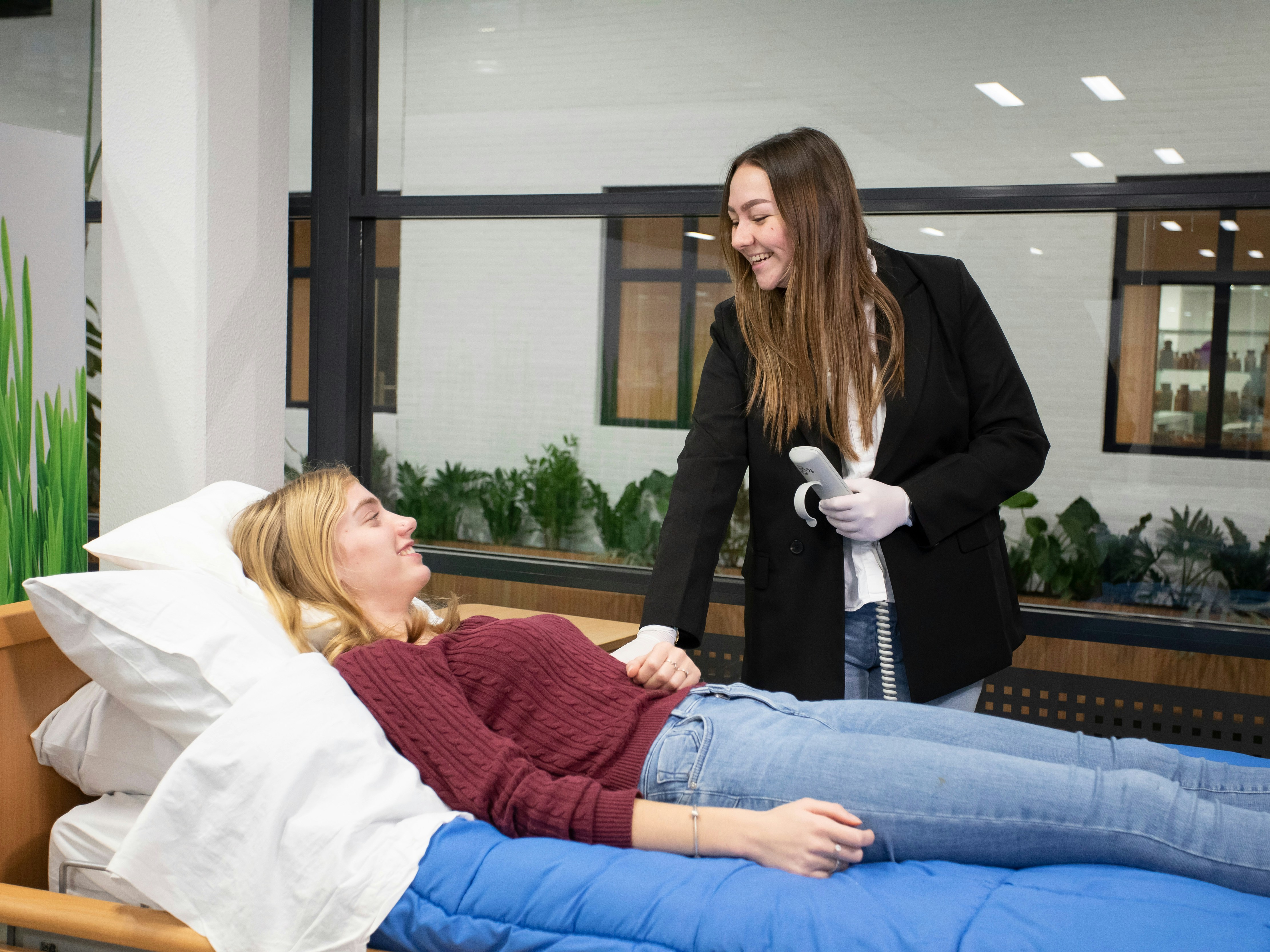 Student staat aan bed met een afstandsbediening in de hand terwijl een andere student op bed ligt