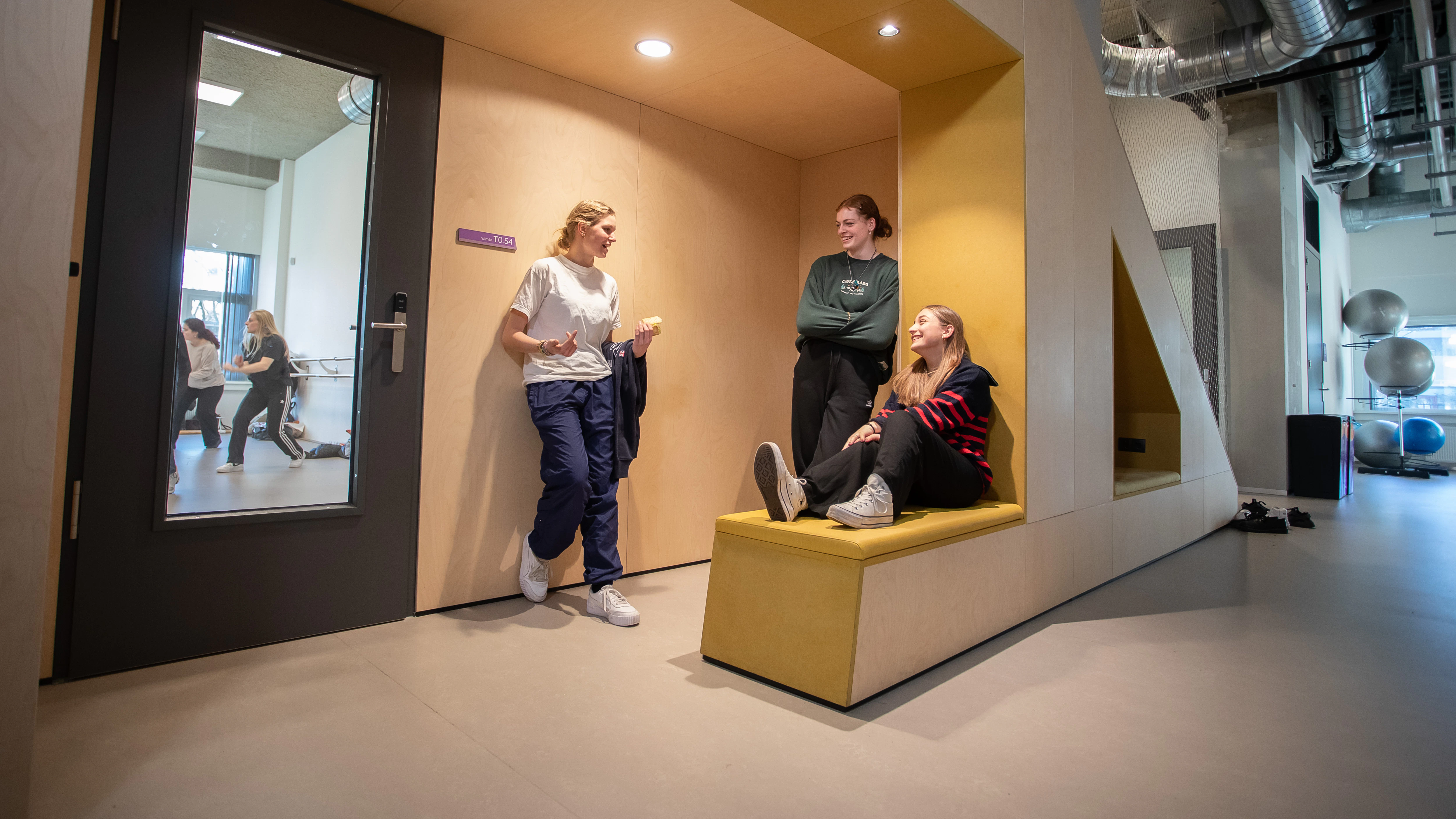 3 studenten zitten op een bank te wachten voor een lokaal