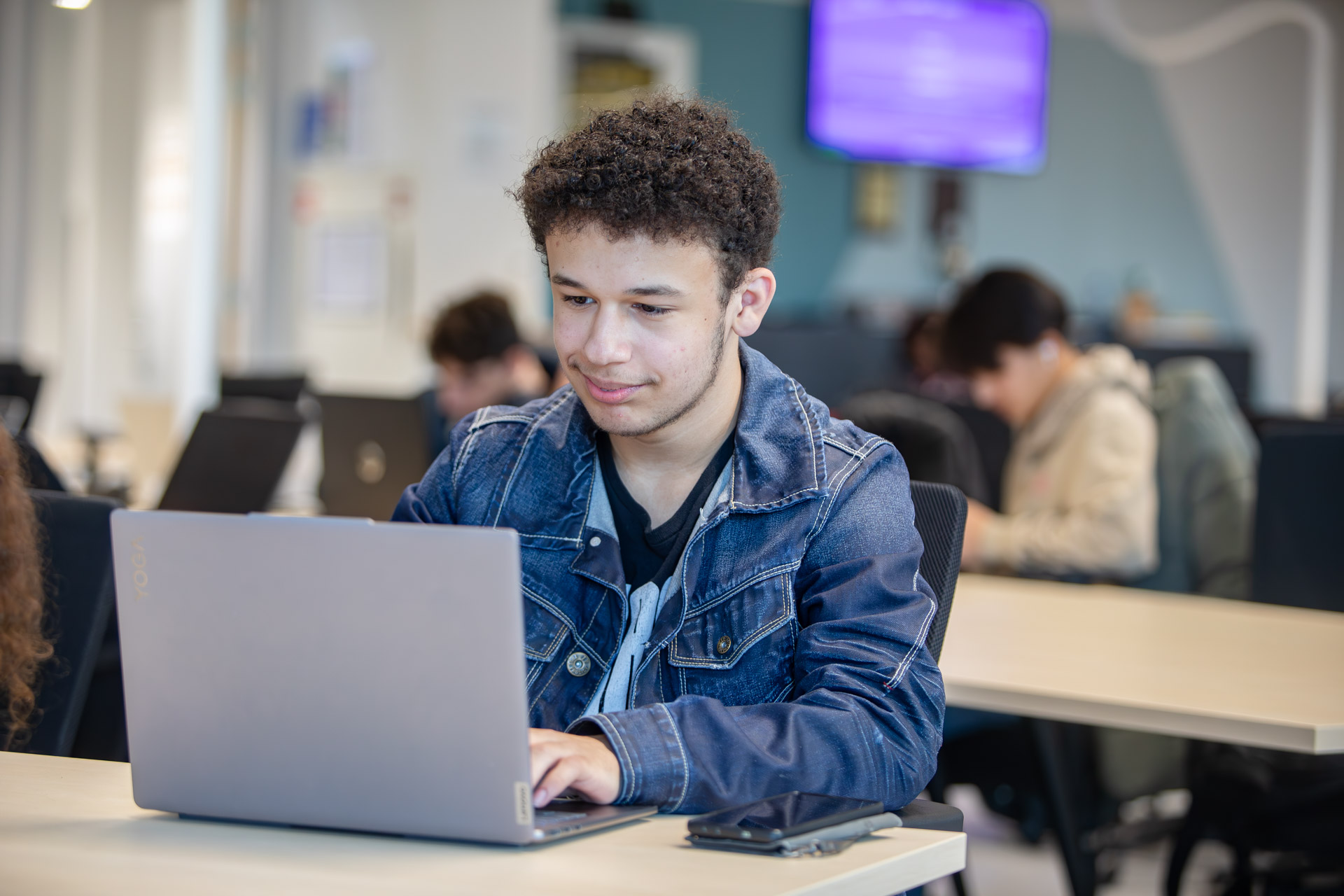 Een jongen in een klaslokaal die aan het werk is achter zijn laptop.