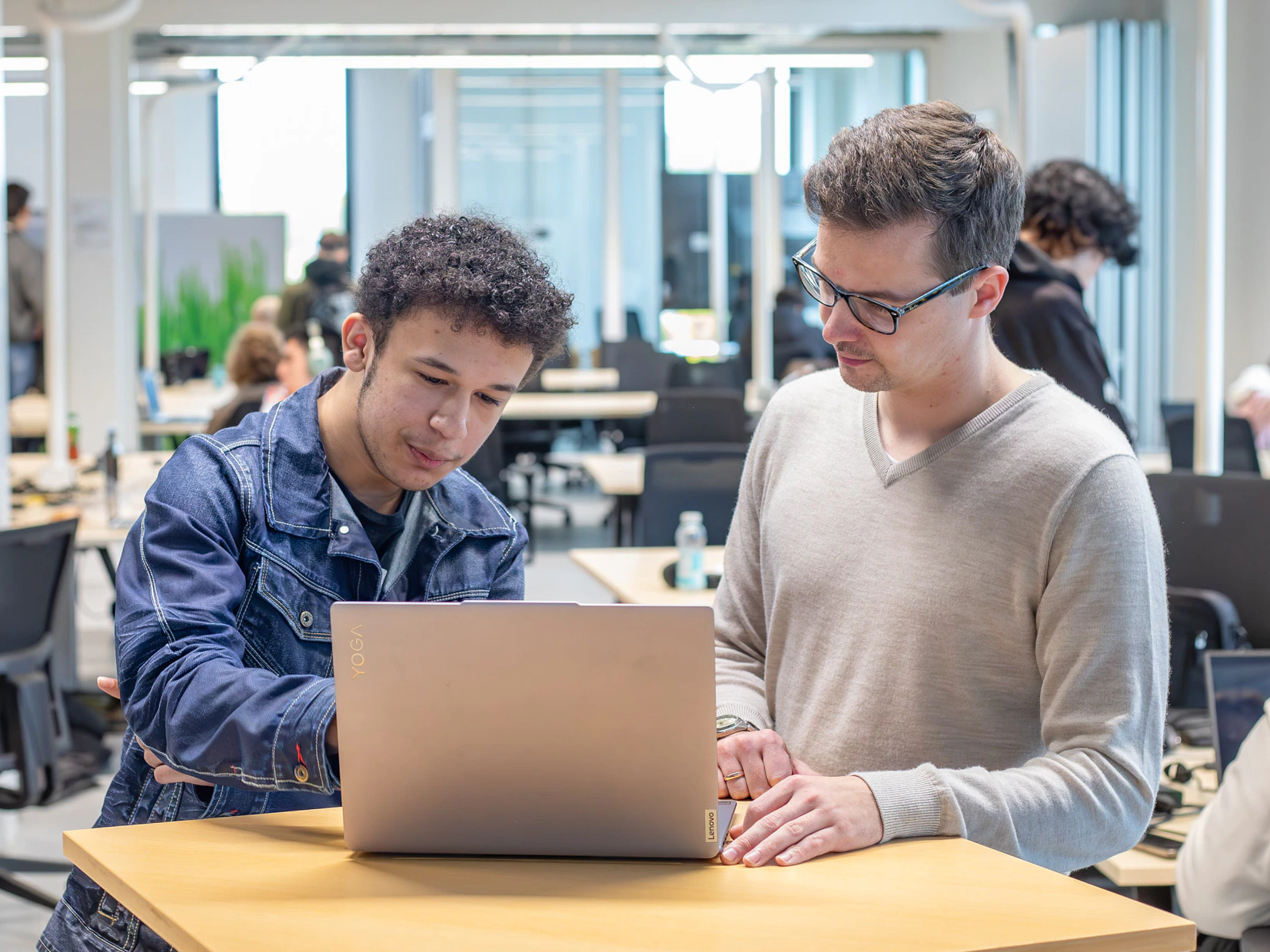 Jongen in een klaslokaal wijst zijn docent iets aan op een laptop.