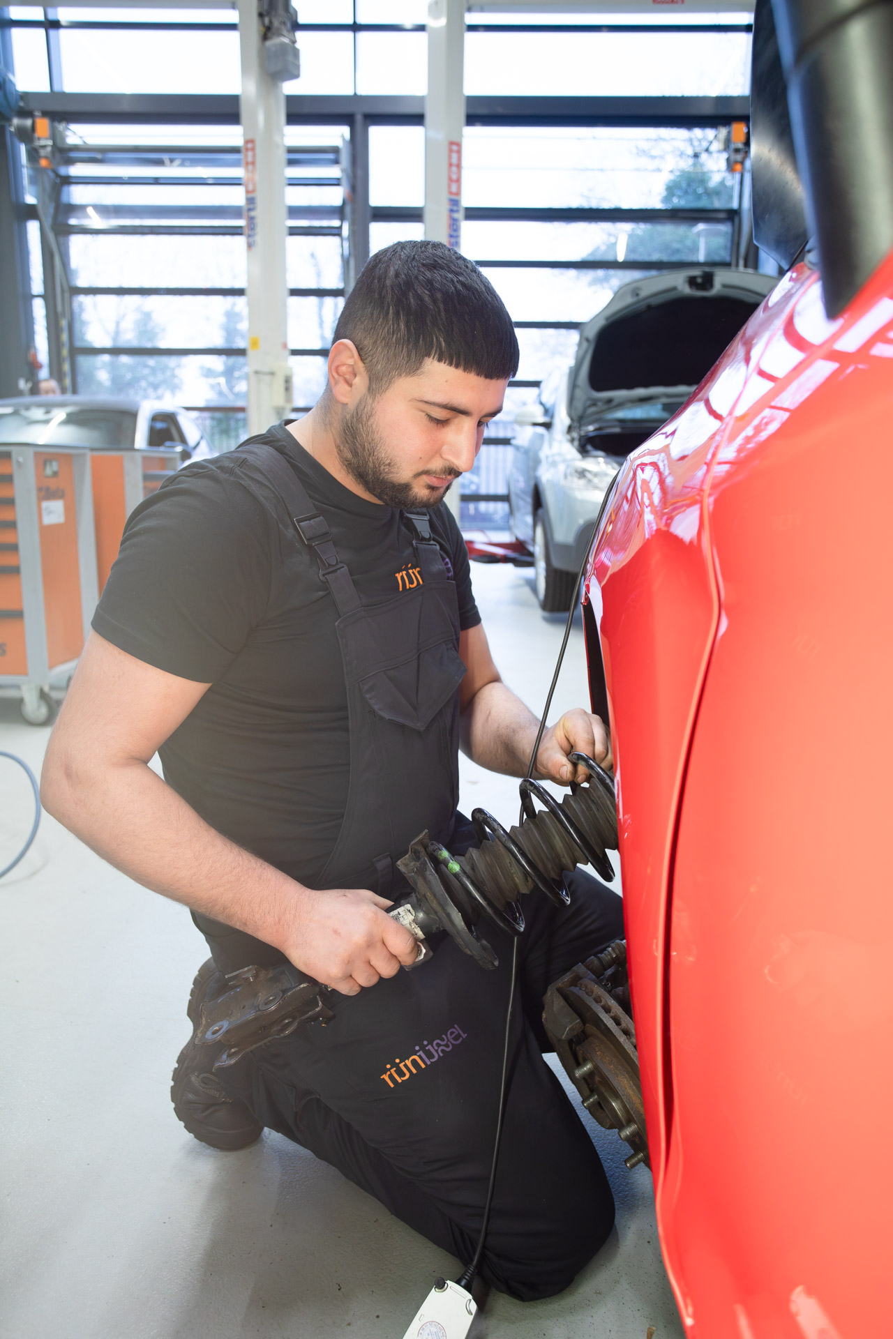 Jongen zit op zijn knieën naast een auto en heeft gereedschap in zijn hand