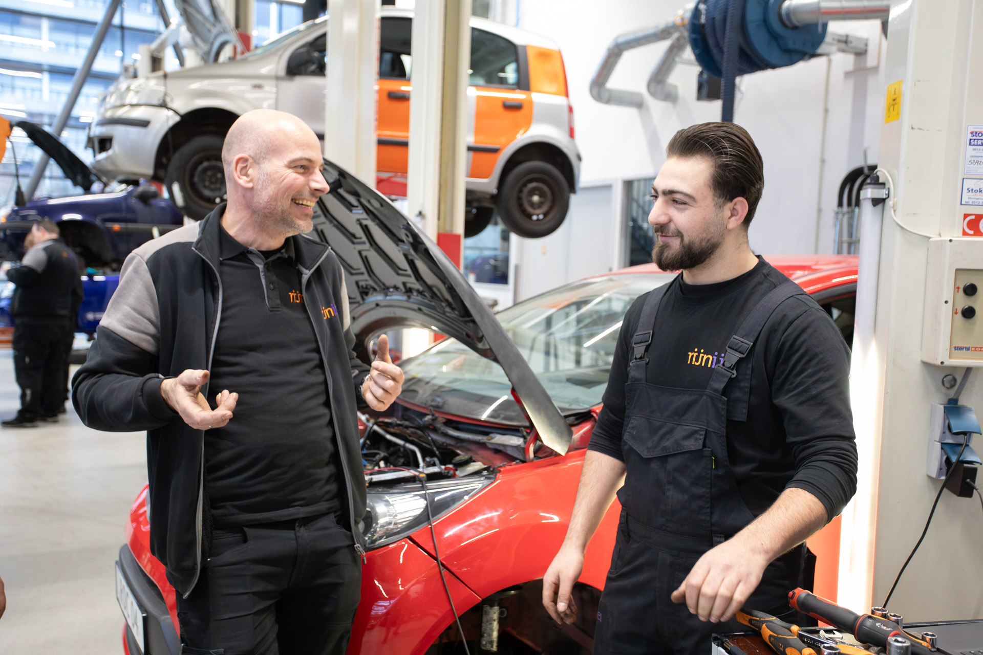 2 mannen kijken elkaar lachend aan terwijl ze voor een auto staan met de motorkap open
