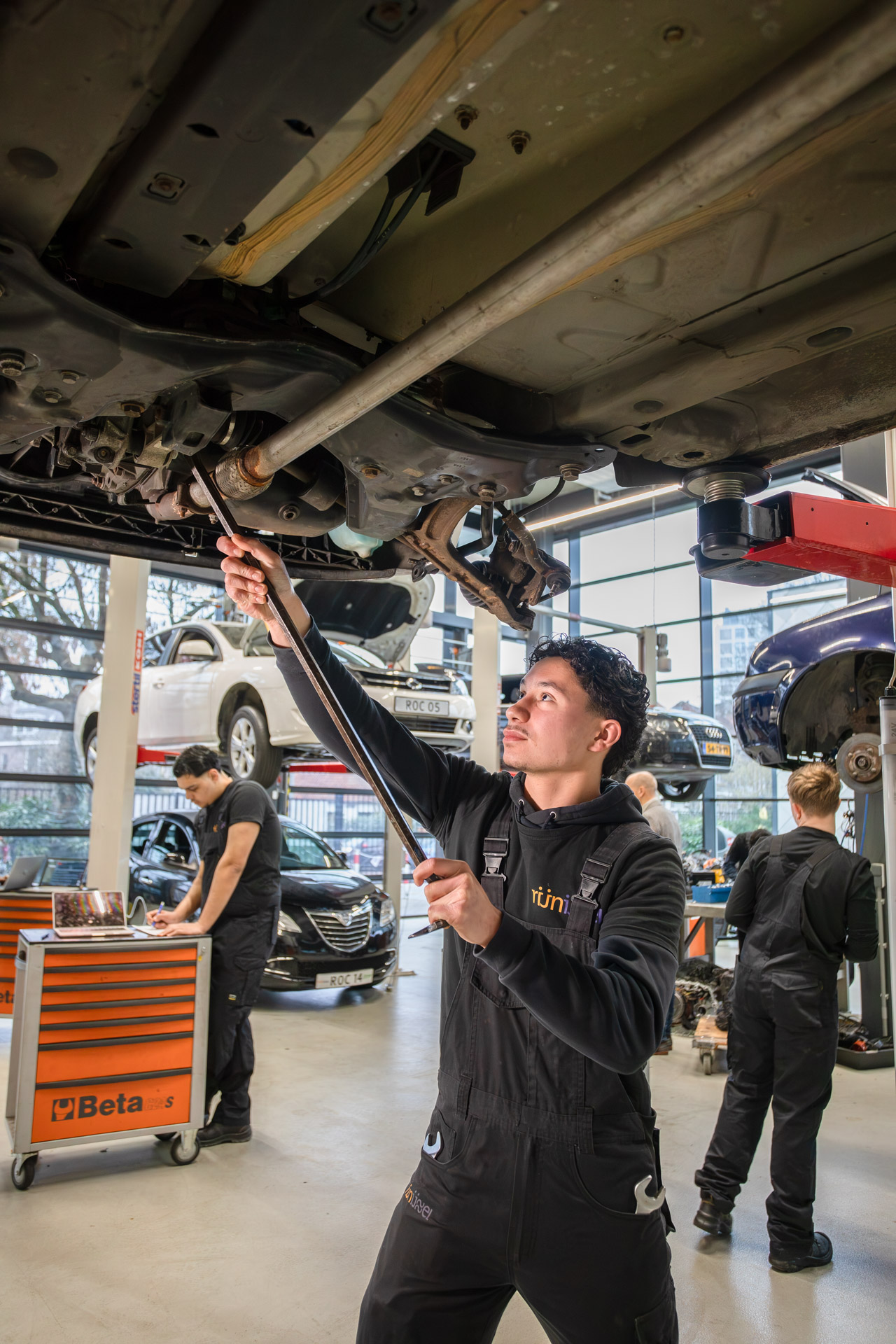 Jongen staat onder een auto die op de brug staat en sleutelt aan de onderkant van de auto