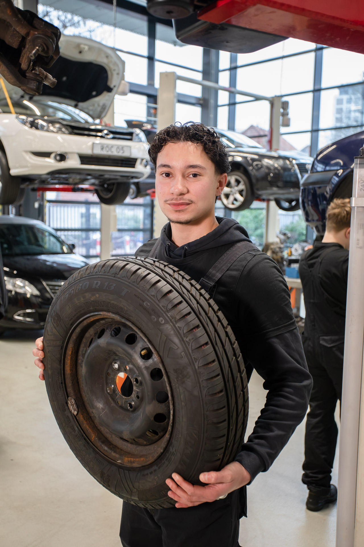 Jongen staat in een garage met een autoband in zijn hand