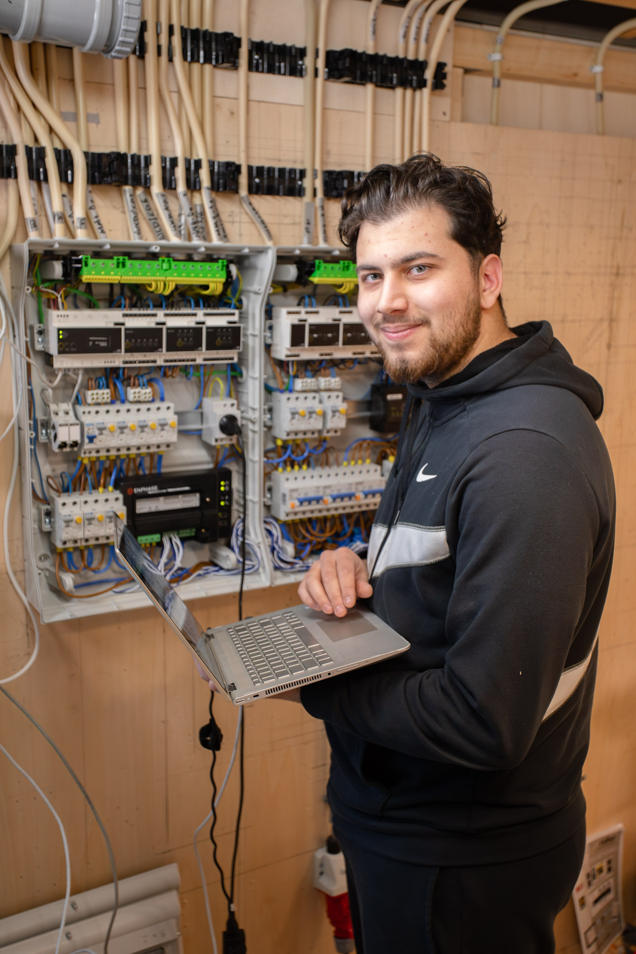 Een jongen poseert voor de camera naast een meterkast met een laptop in zijn handen.