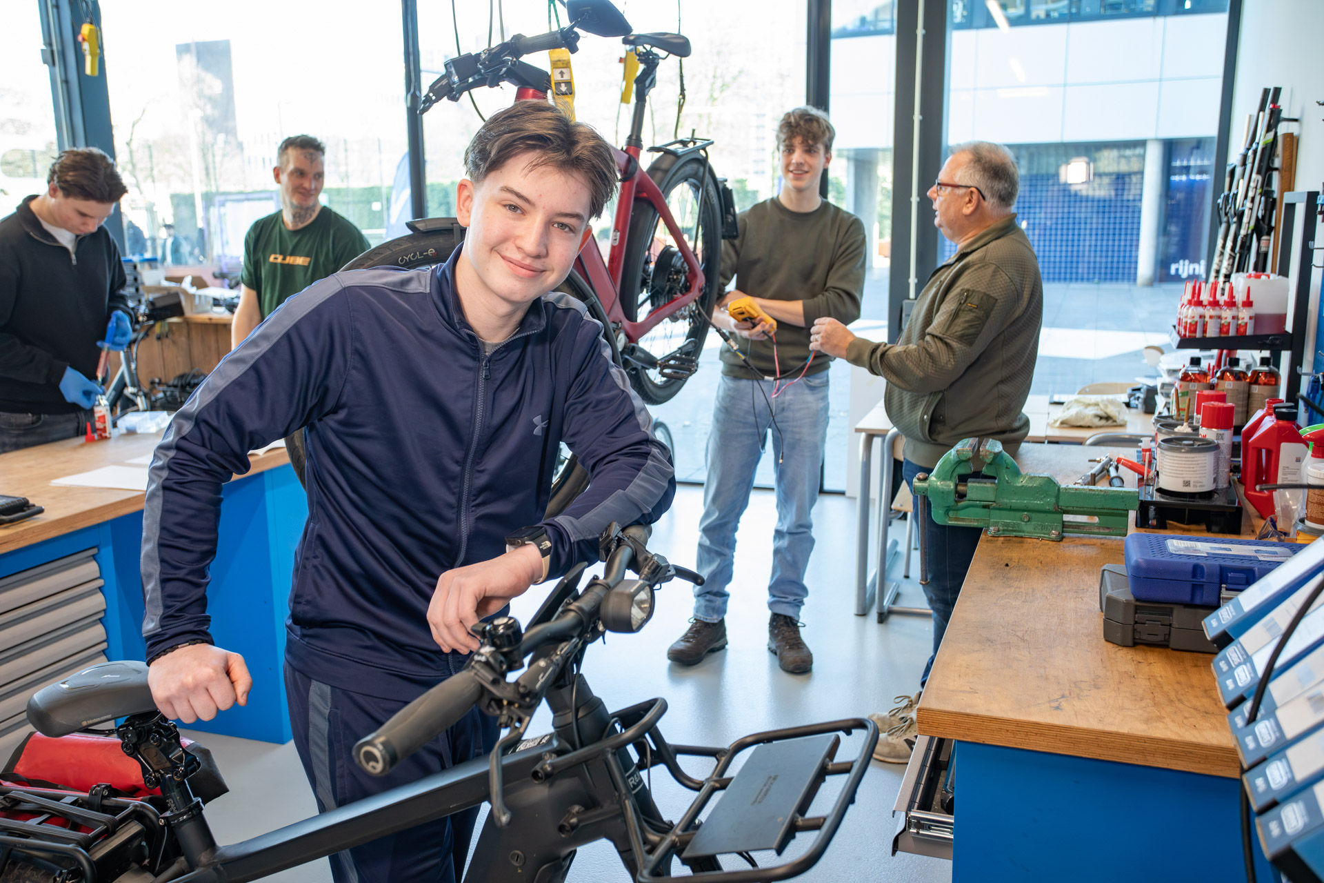 Een jongen in een fietsenwerkplaat leunt op een fiets terwijl hij poseert voor de camera.