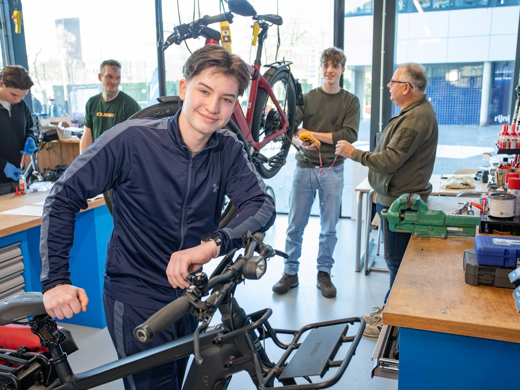 Een jongen in een fietsenwerkplaat leunt op een fiets terwijl hij poseert voor de camera.