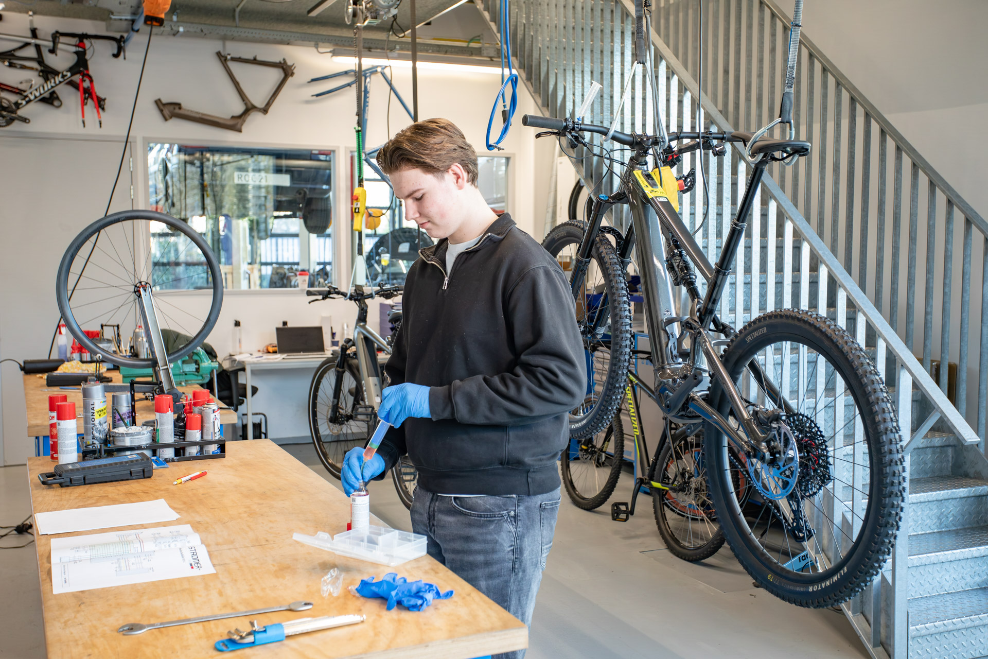 Een jongen in een fietsenwerkplaats die olie uit een flesje haalt met een spuitje.