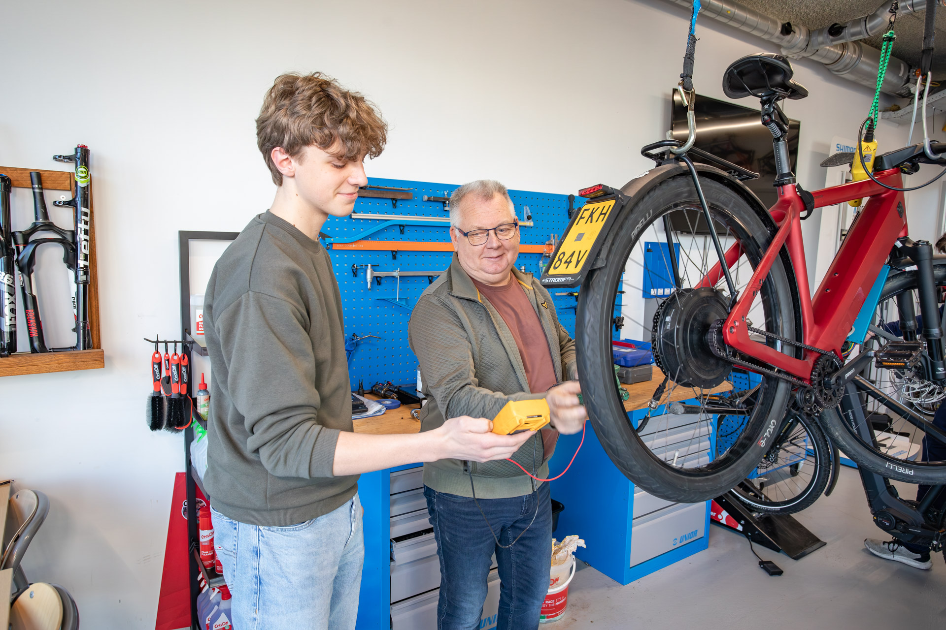 Een jongen in een fietsenwerkplaats die uitleg krijgt van een docent bij een fiets.